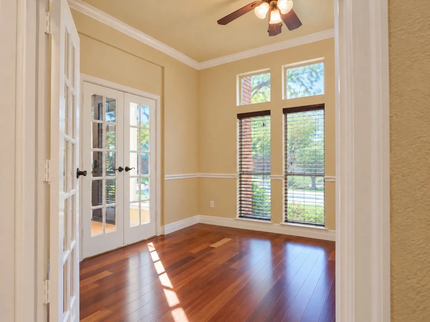 Double French doors, wood-finish flooring, crown molding, double windows with blinds, and a ceiling fan with light fixture