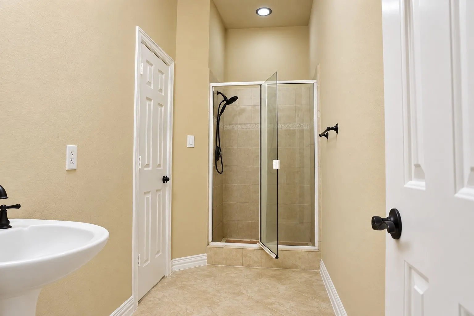 Pedestal sink with a matte black faucet, walk-in shower with glass enclosure, recessed lighting, and tile flooring