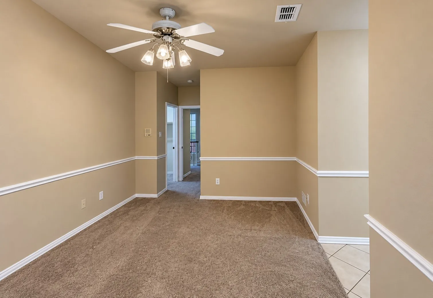 Carpeted room featuring a ceiling fan with integrated lighting, chair rail molding, and a neutral color palette