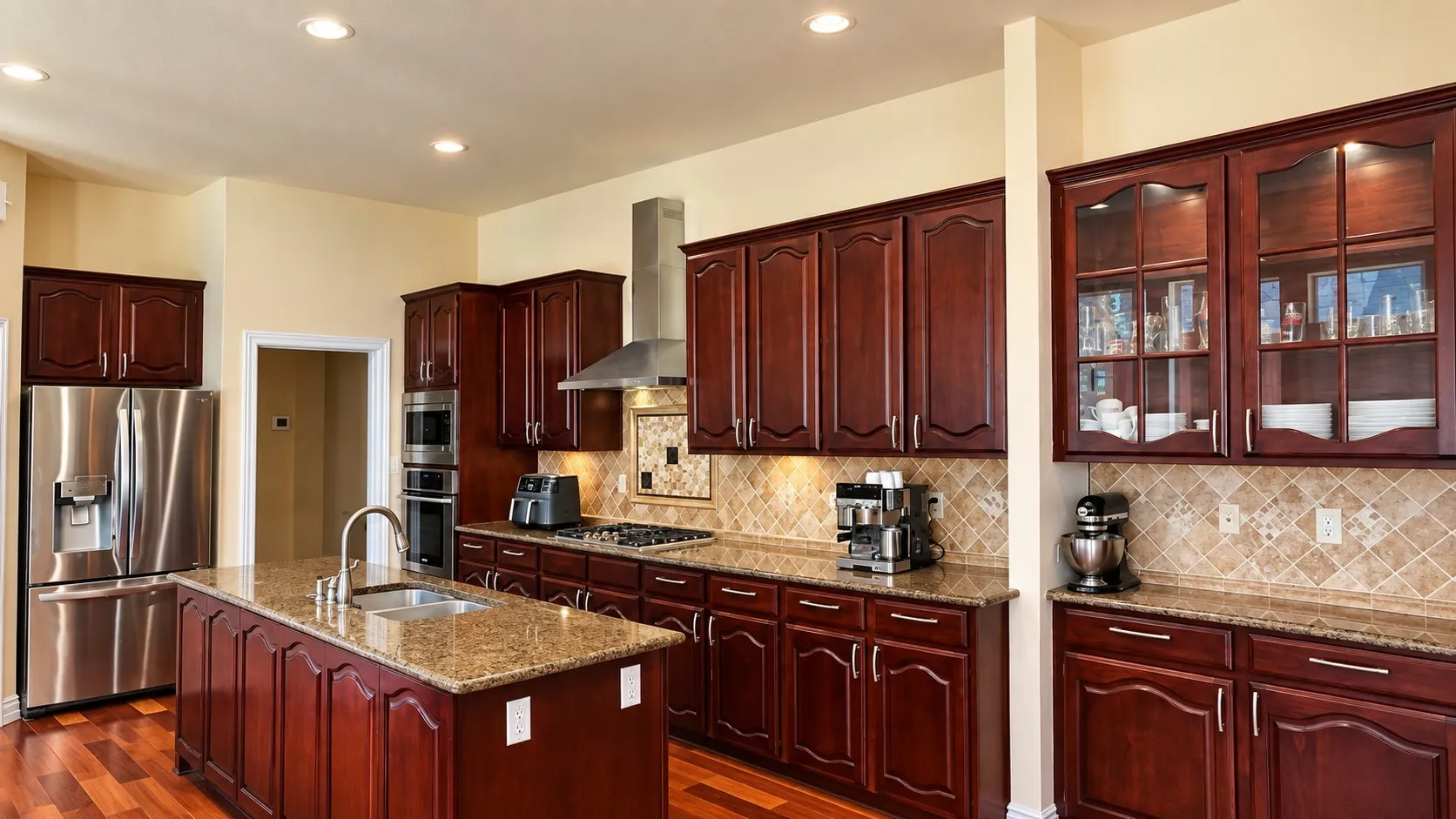 Kitchen featuring wood-finish flooring, an island with an integrated sink, granite countertops, and stainless steel appliances