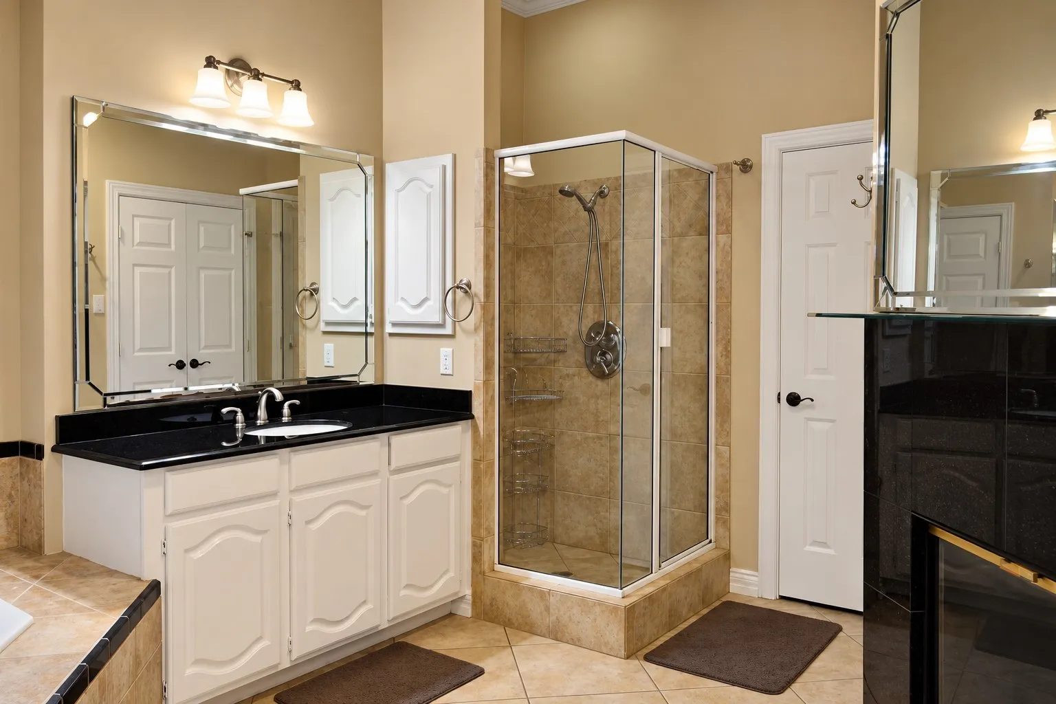 Tile flooring, white vanity with black countertop, glass-enclosed shower, wall-mounted vanity lights, and a large wall mirror