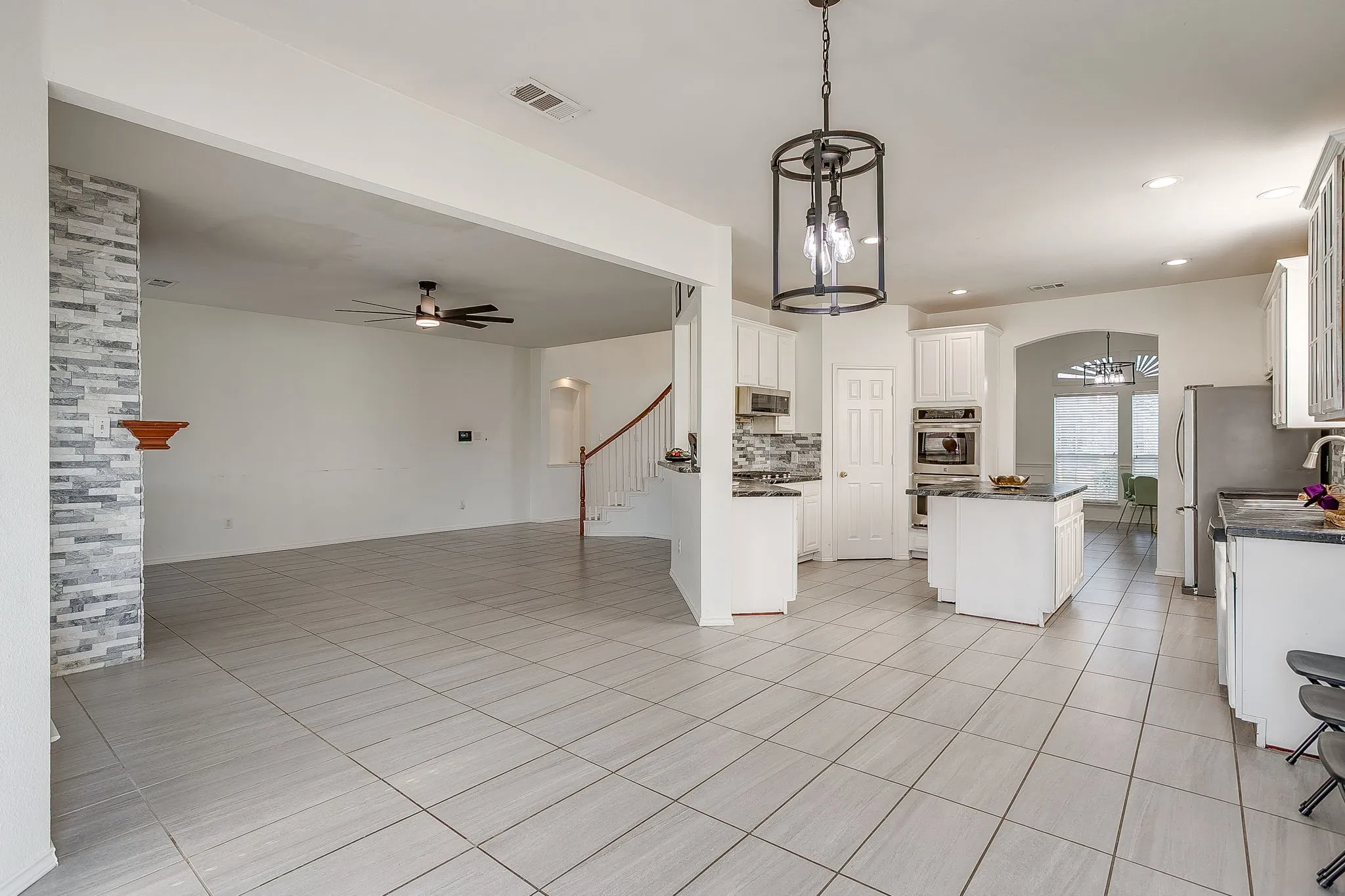 Large tile flooring, ceiling fan, staircase with wood handrail, and pass-through window