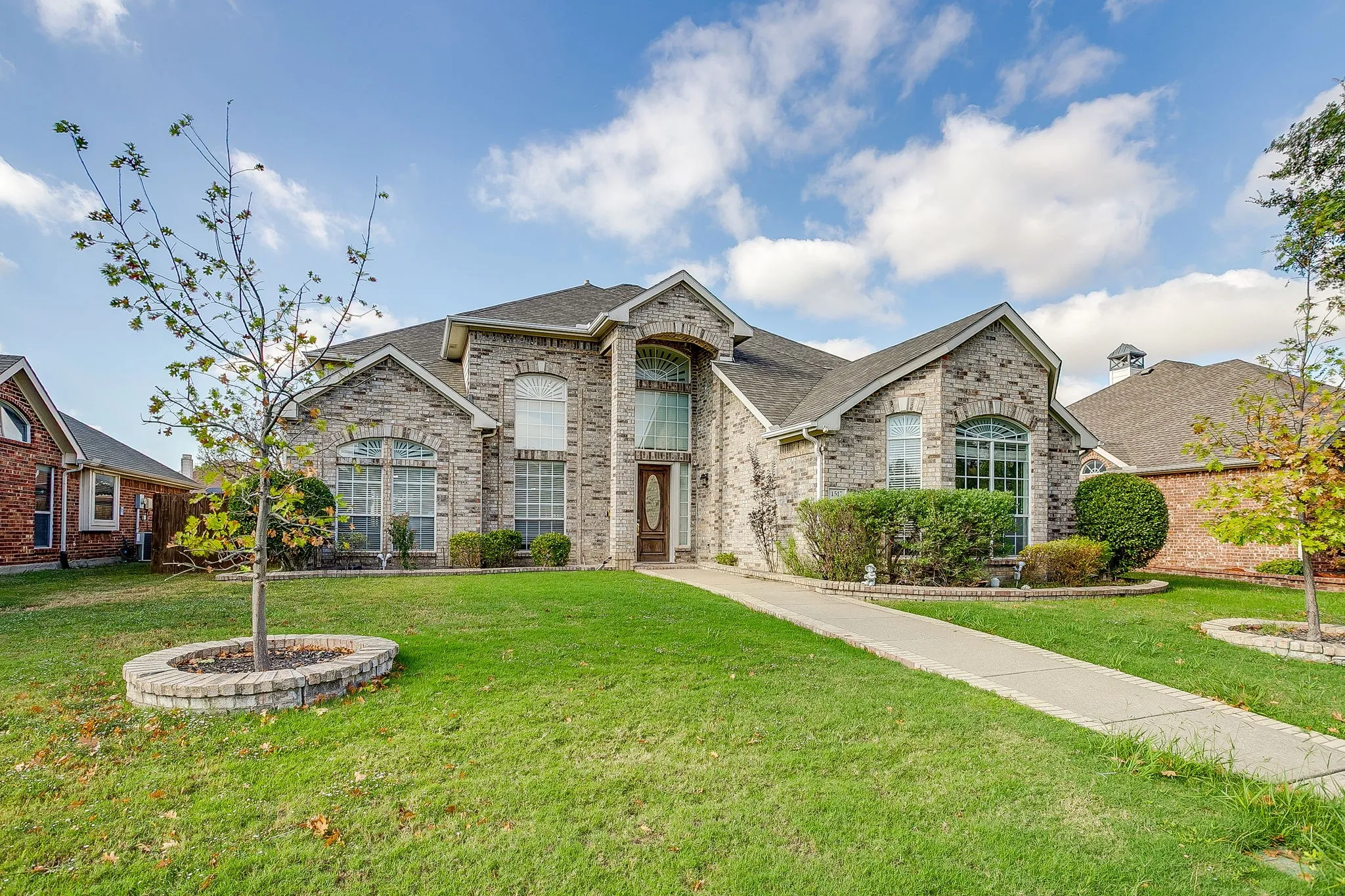 Multi-gabled brick exterior featuring arched window detailing, an arched entry, a concrete walkway with paver edging, and stone-bordered landscaping