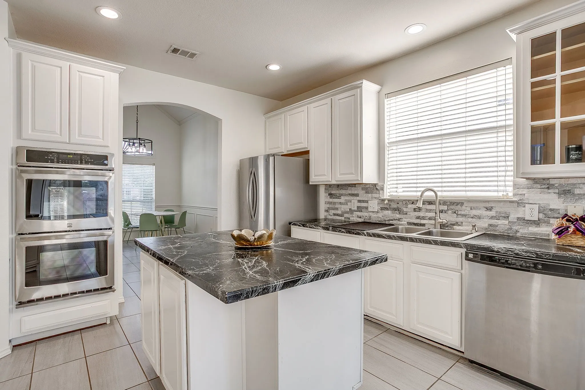Kitchen featuring a center island , white cabinetry, stacked-stone backsplash, stainless steel built-in microwave, gas stove