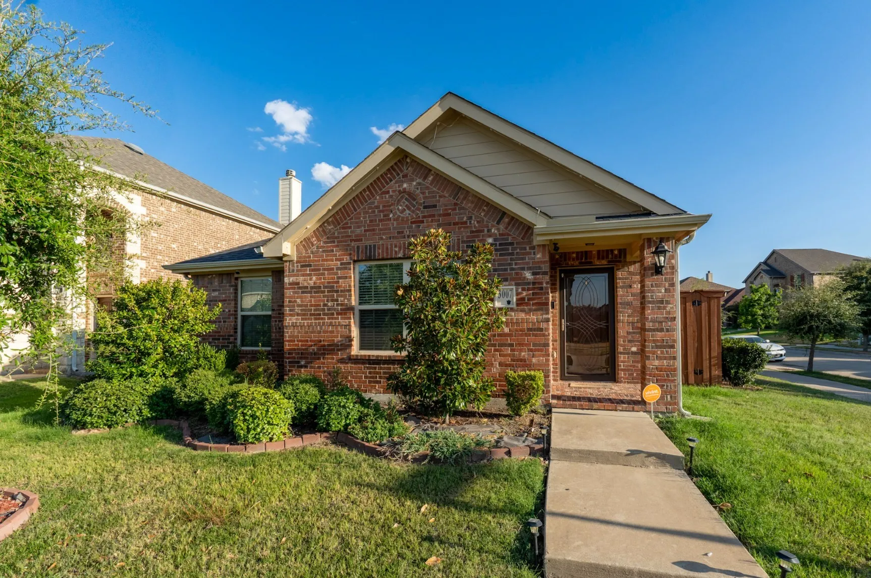 Single-story residence featuring a brick exterior, gable roofline, covered entryway with a decorative glass-panel front door, and manicured landscaping