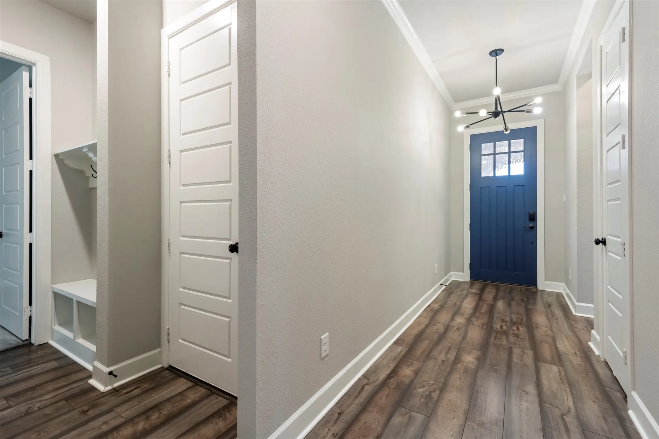 Entryway featuring wood-finish flooring, a multi-pane glass panel front door, contemporary multi-arm chandelier, and built-in mudroom bench with shelving