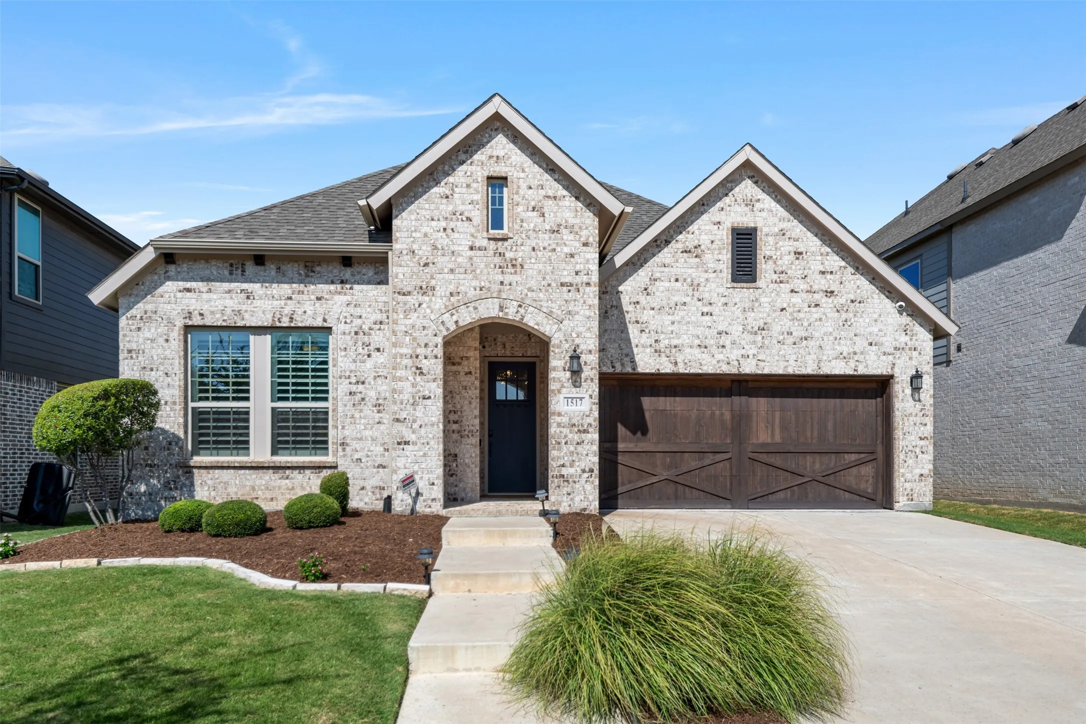 Brick exterior featuring a multi-gabled roofline, a dark-stained wood garage door with decorative cross-bracing, and a covered entryway