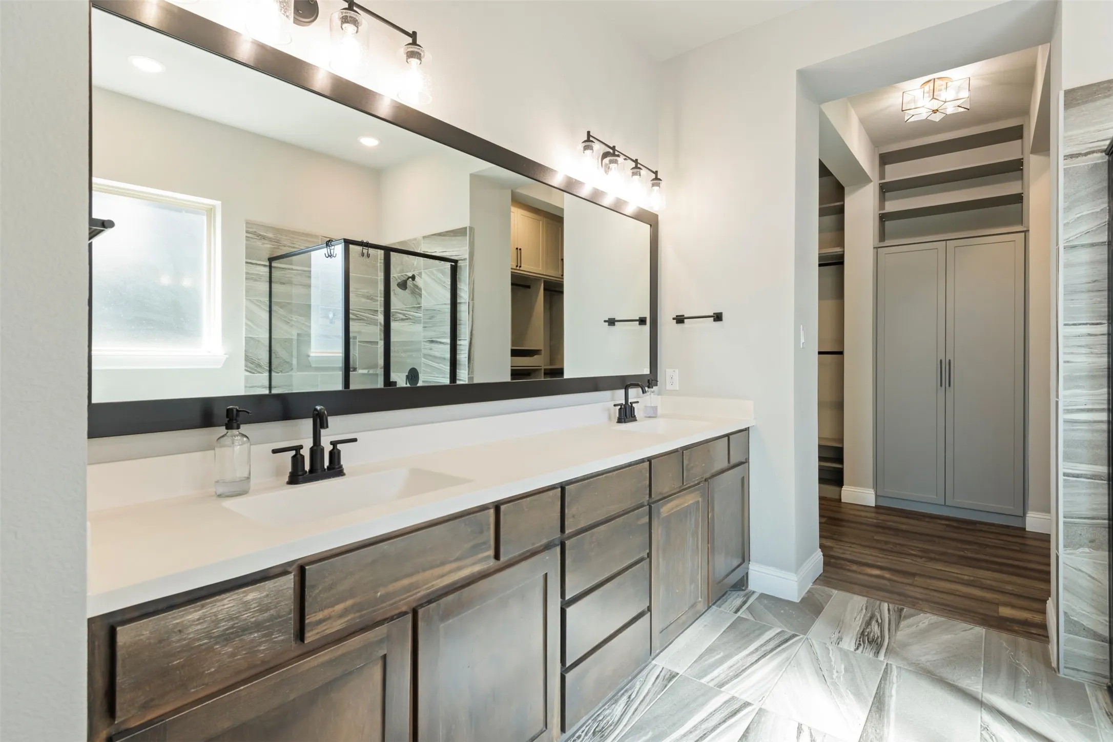 Dual-sink vanity with matte black fixtures, quartz countertop, full-width framed mirror, stone-finish flooring, and built-in cabinetry