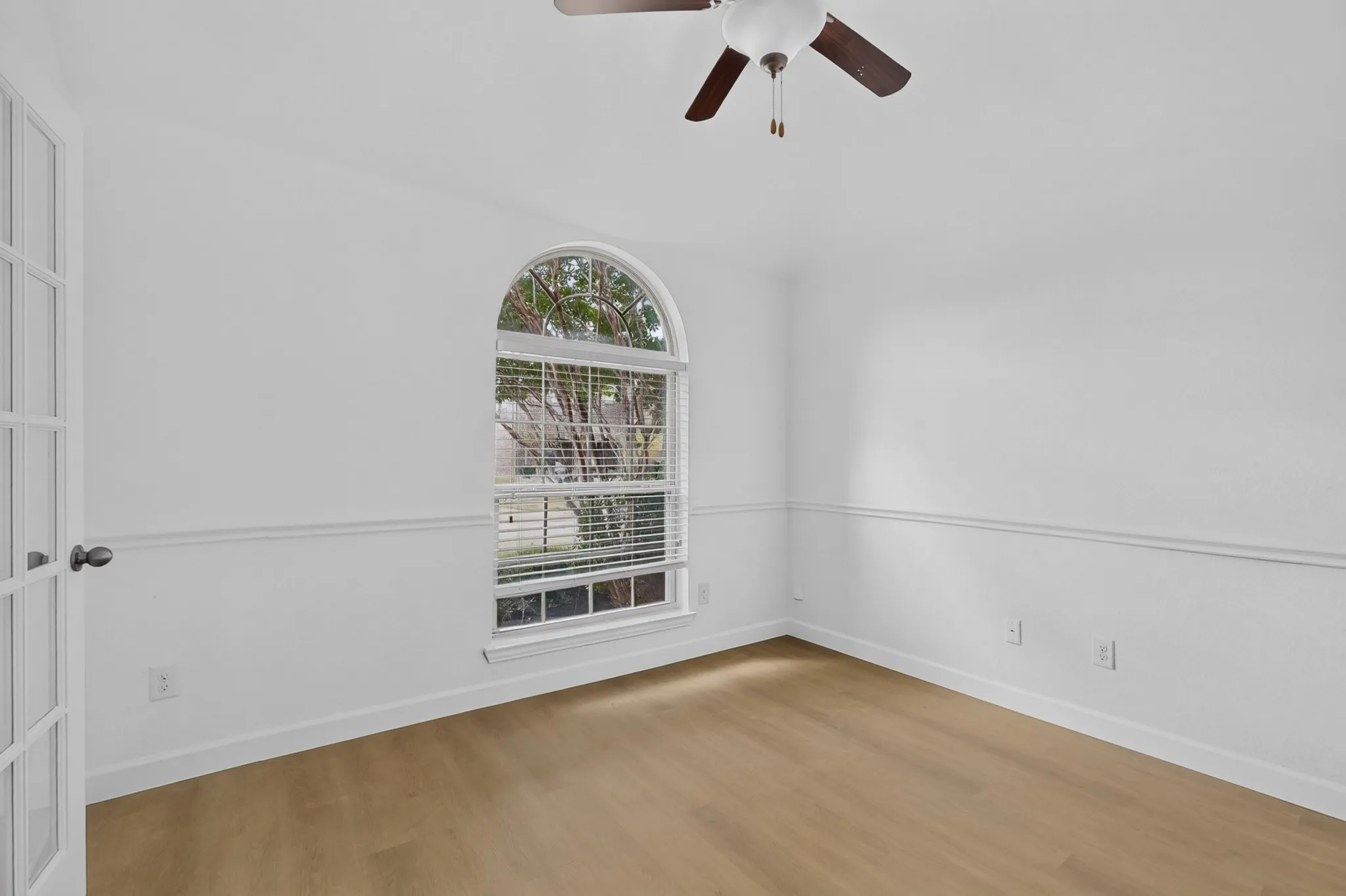 Room featuring wood-finish flooring, an arched window, chair rail molding, a multi-pane glass door, and a ceiling fan