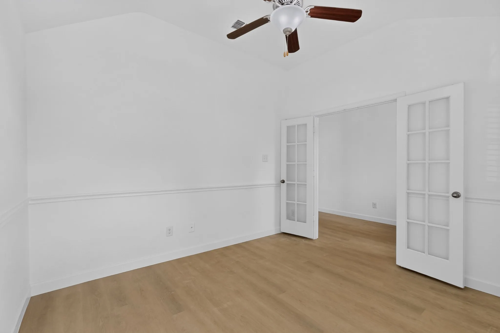 Vaulted ceiling room featuring wood-finish flooring, white chair rail molding, and a ceiling fan