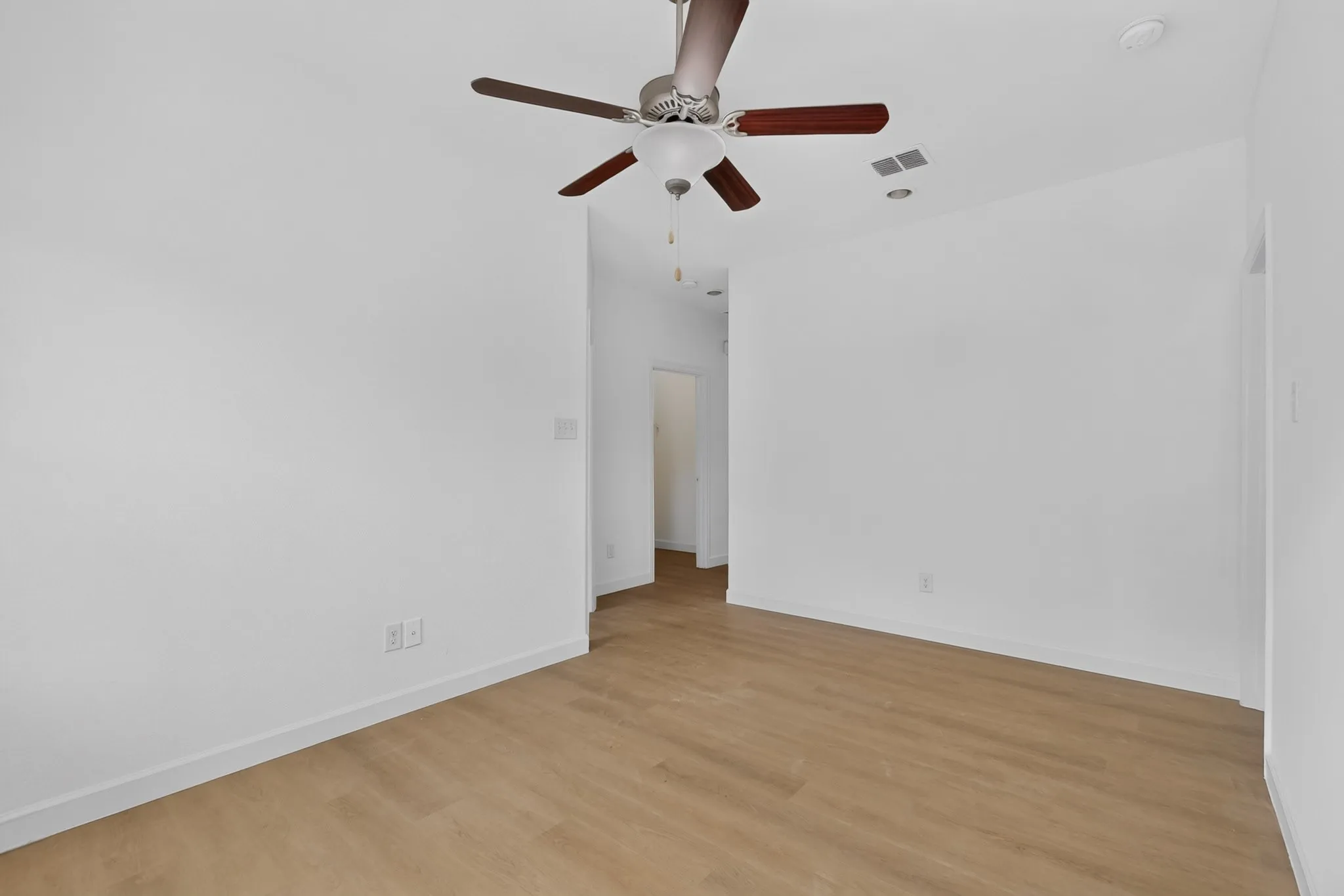 Neutral interior featuring wood-finish flooring, white walls, and a ceiling fan with integrated lighting