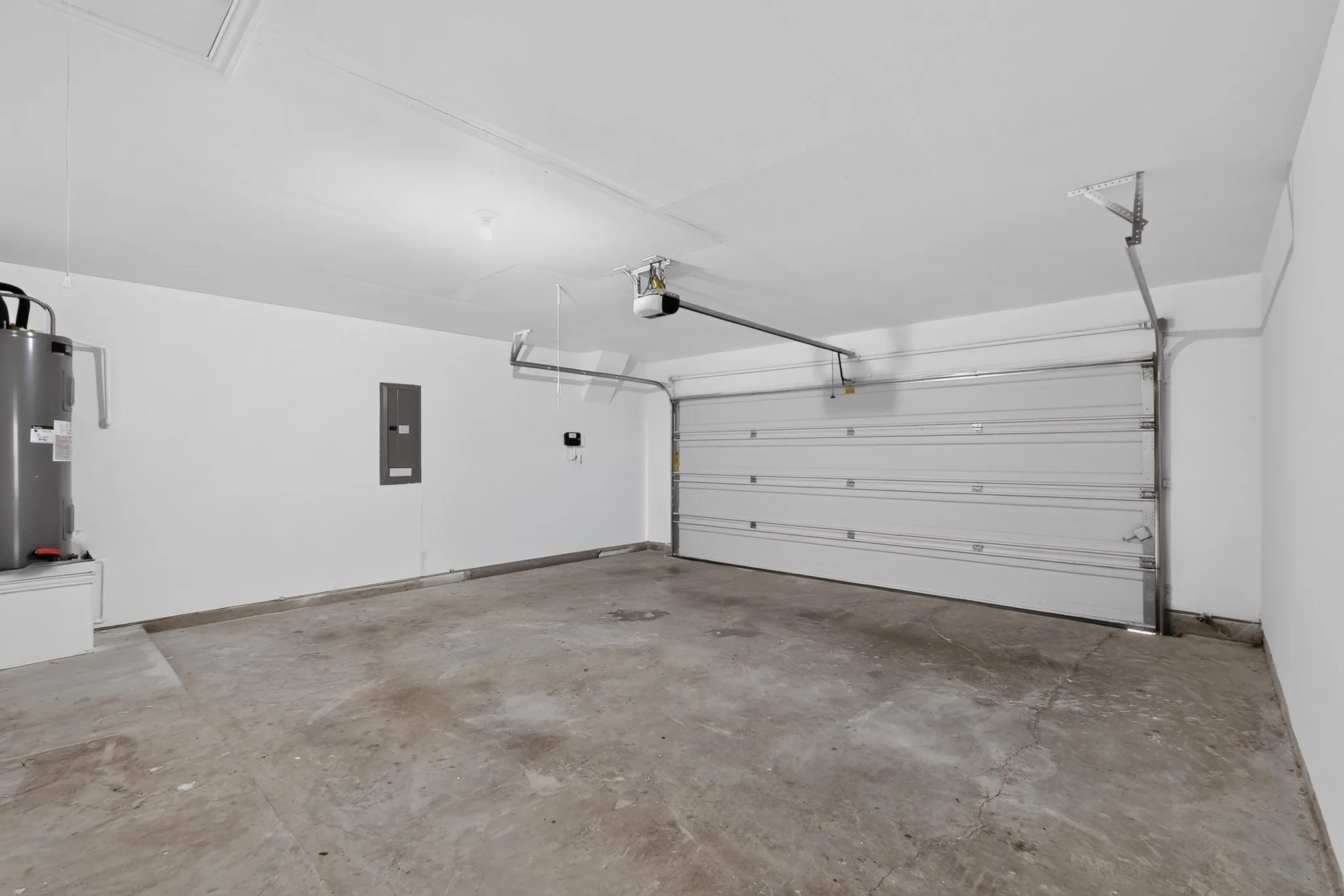 Enclosed garage featuring concrete flooring, white walls, overhead door opener, and integrated electrical panel