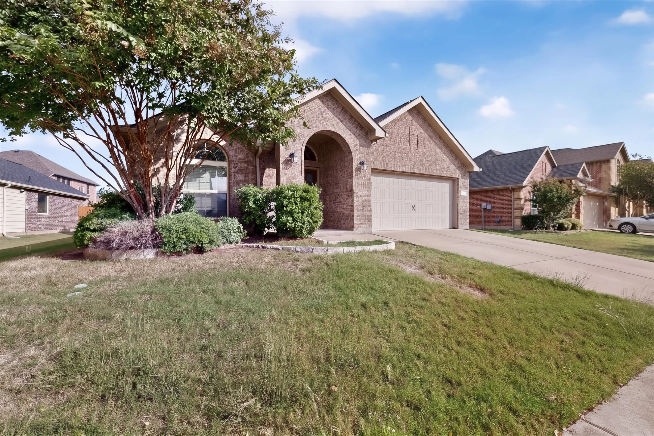 Brick exterior featuring an arched entryway, gabled rooflines, two-car garage, and a front yard with mature landscaping
