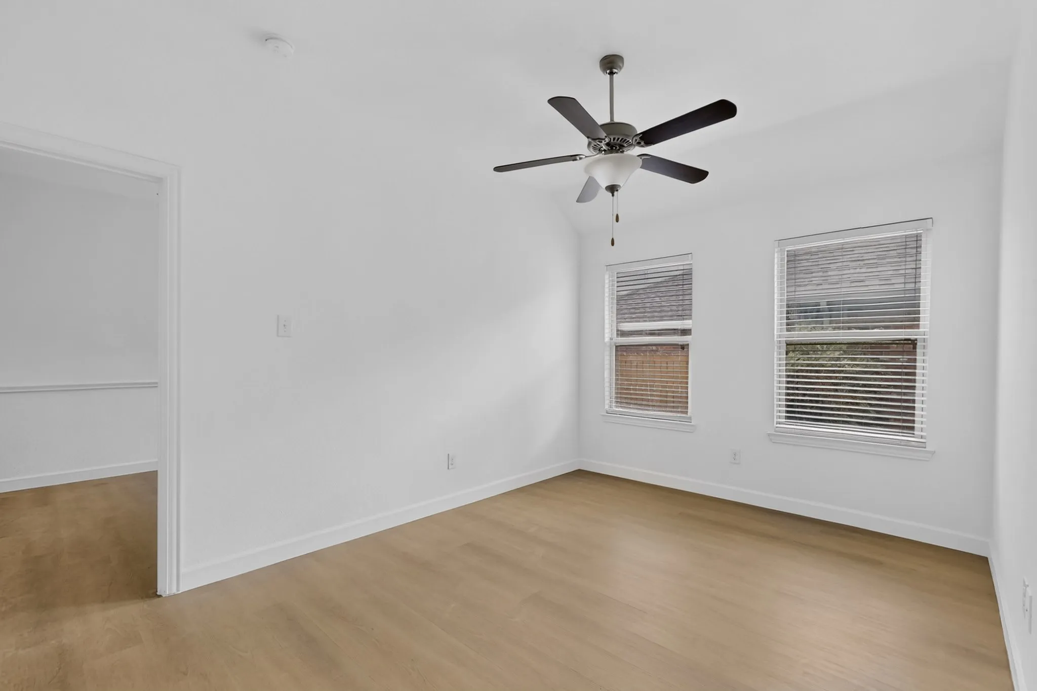 Interior room featuring wood-finish flooring, two dual-pane windows with horizontal blinds, a vaulted ceiling, and a ceiling-mounted fan with integrated lighting
