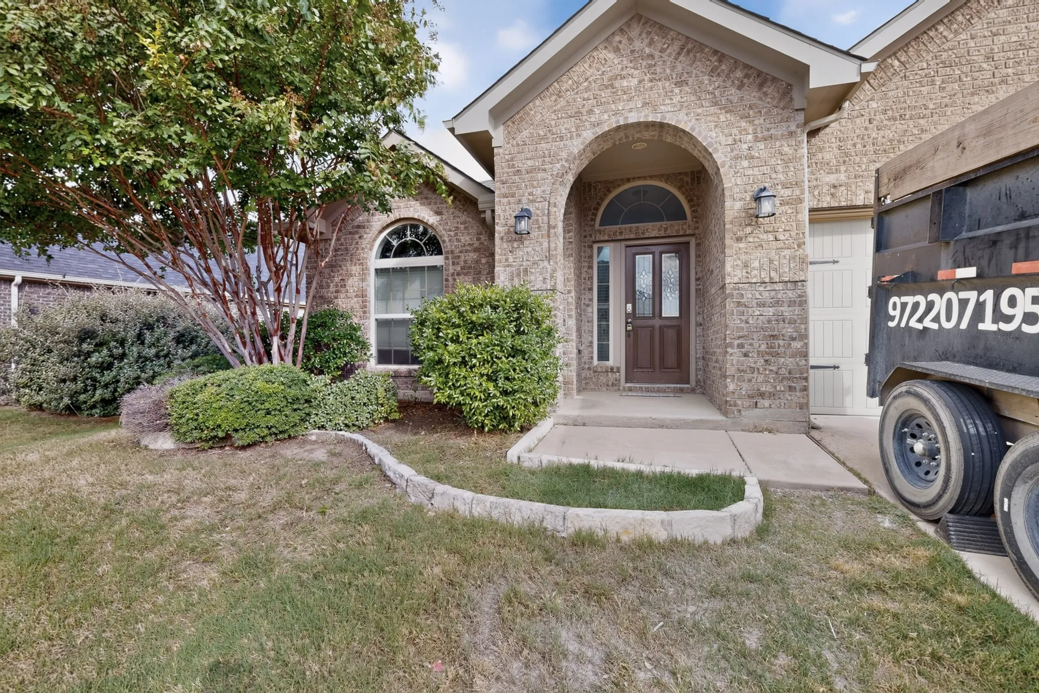 Brick exterior featuring an arched entryway, stone-bordered landscaping, and a paneled front door with decorative glass inserts