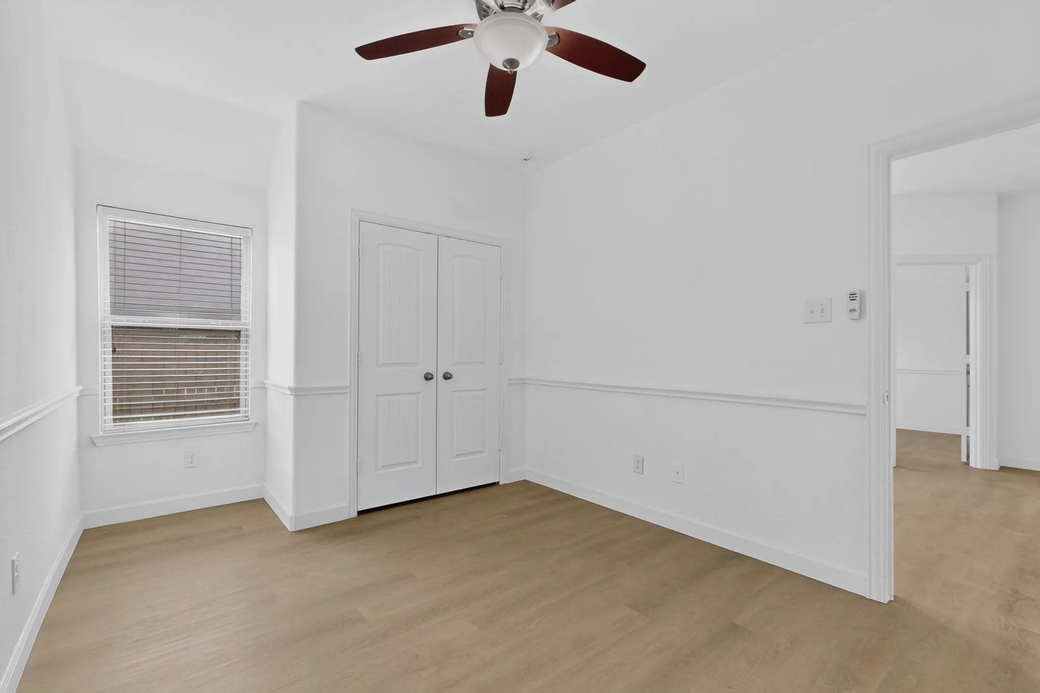 Room featuring wood-finish flooring, chair rail molding, double-door closet, ceiling fan with integrated lighting, and a window with horizontal blinds