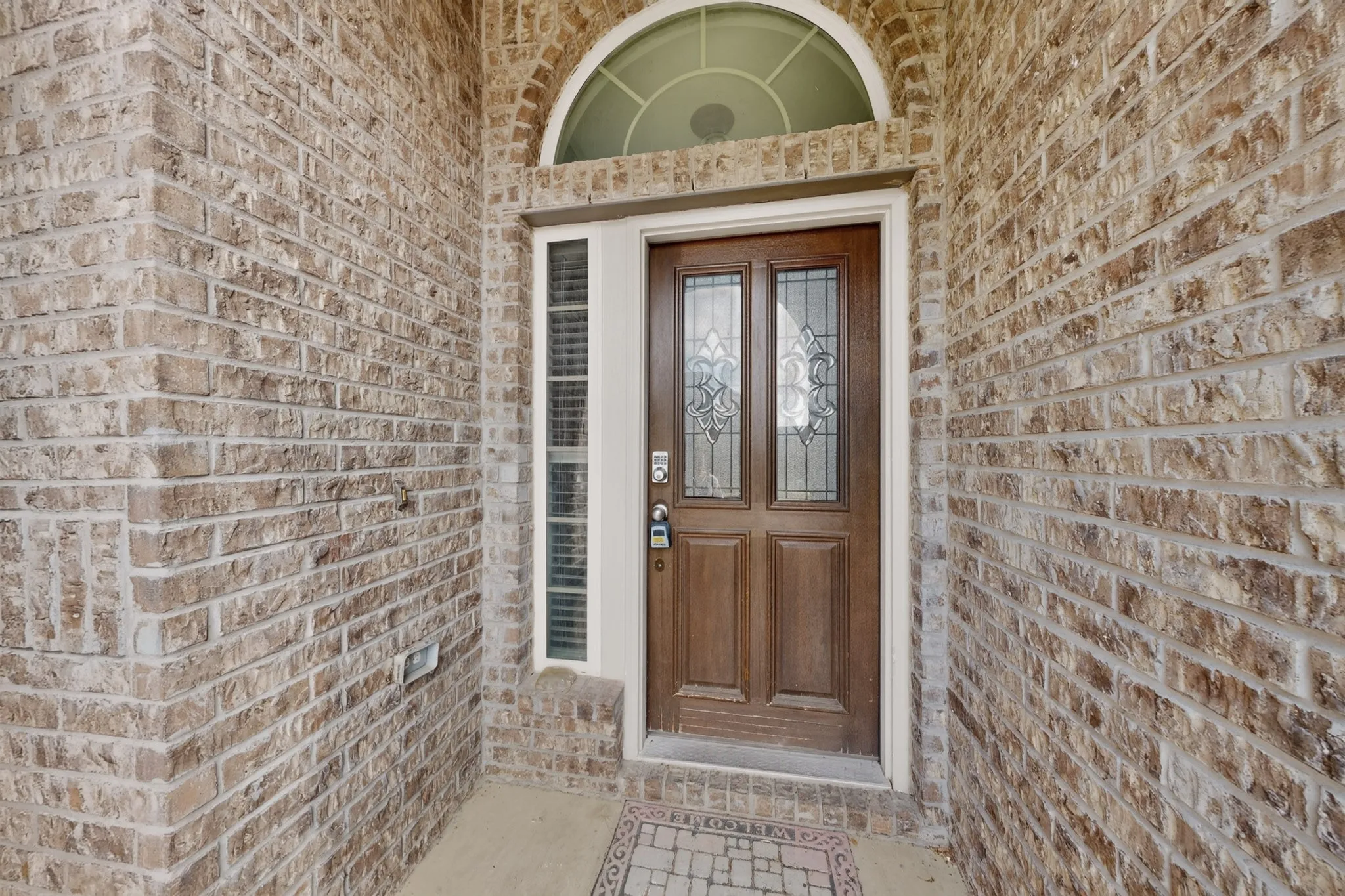 Exterior entryway featuring a brick facade, arched transom window, side light, and solid wood door with decorative glass panels
