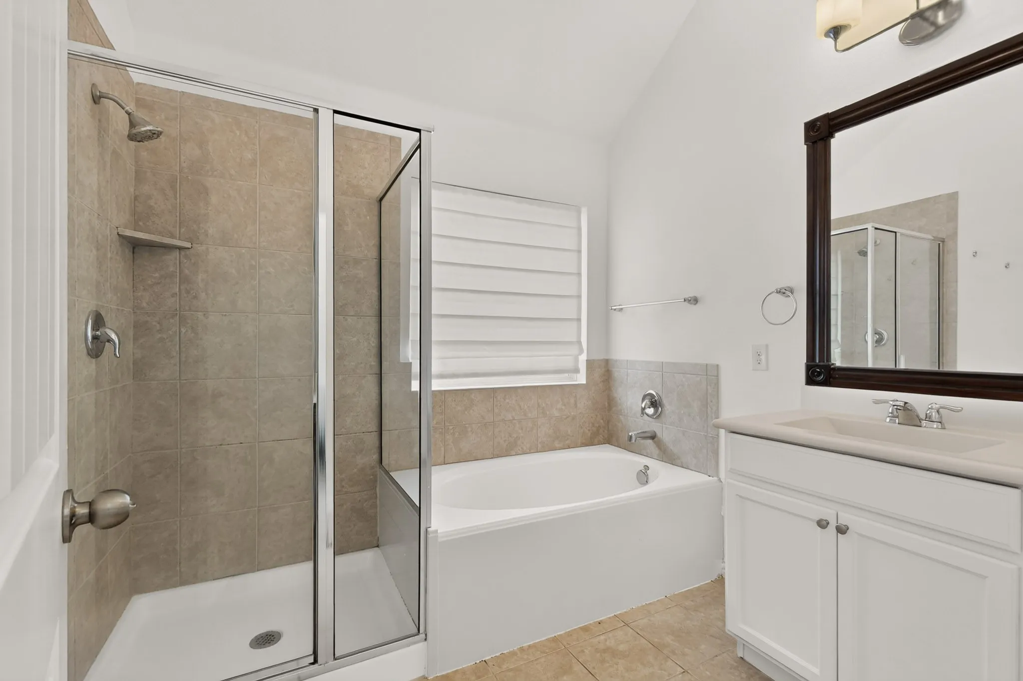 Bathroom featuring a glass-enclosed shower, built-in soaking tub with tile surround, white vanity cabinet, and vaulted ceiling