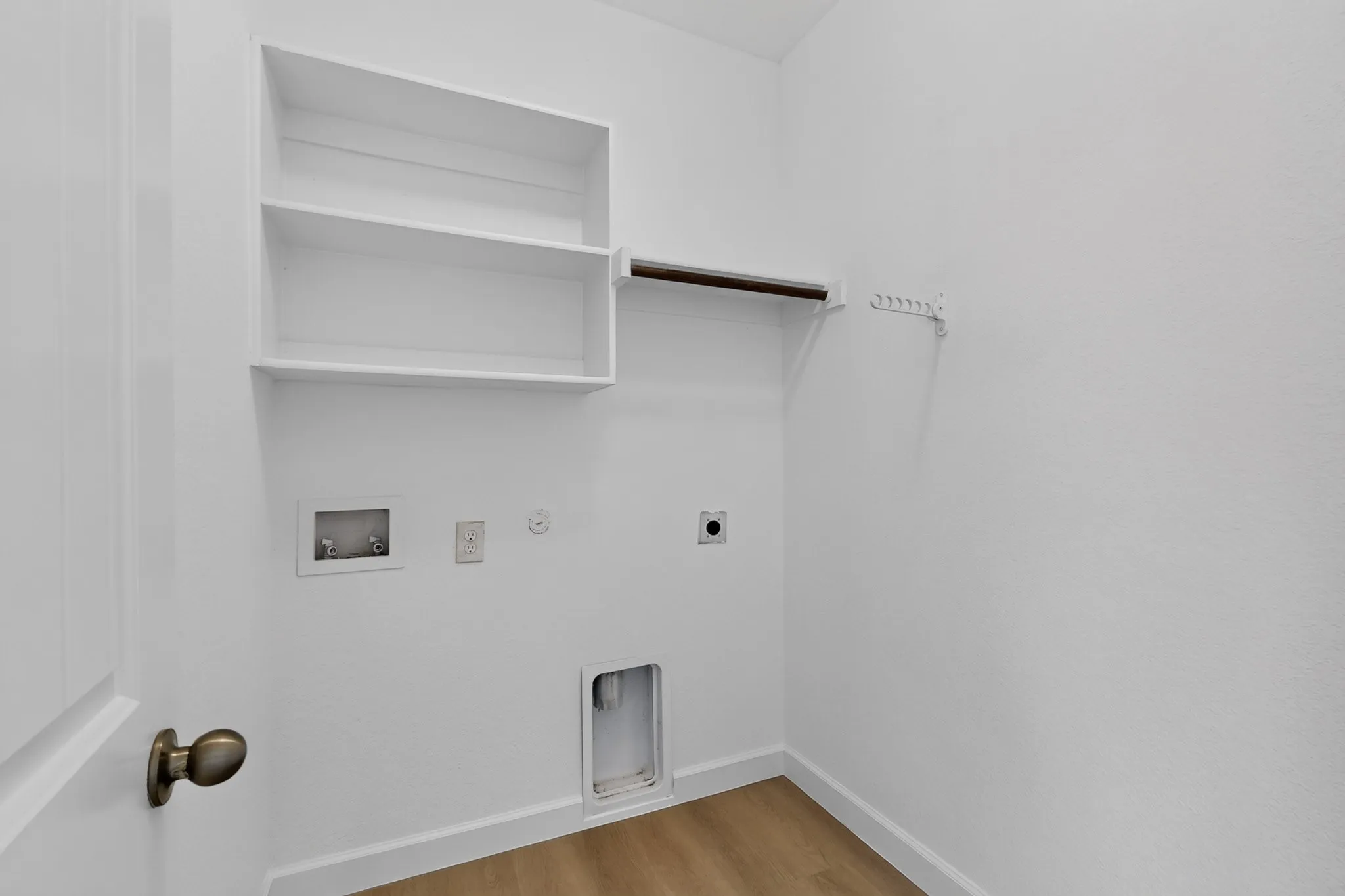 Utility area featuring wood-finish flooring, white built-in shelving, a wall-mounted garment rod, and plumbing hookups