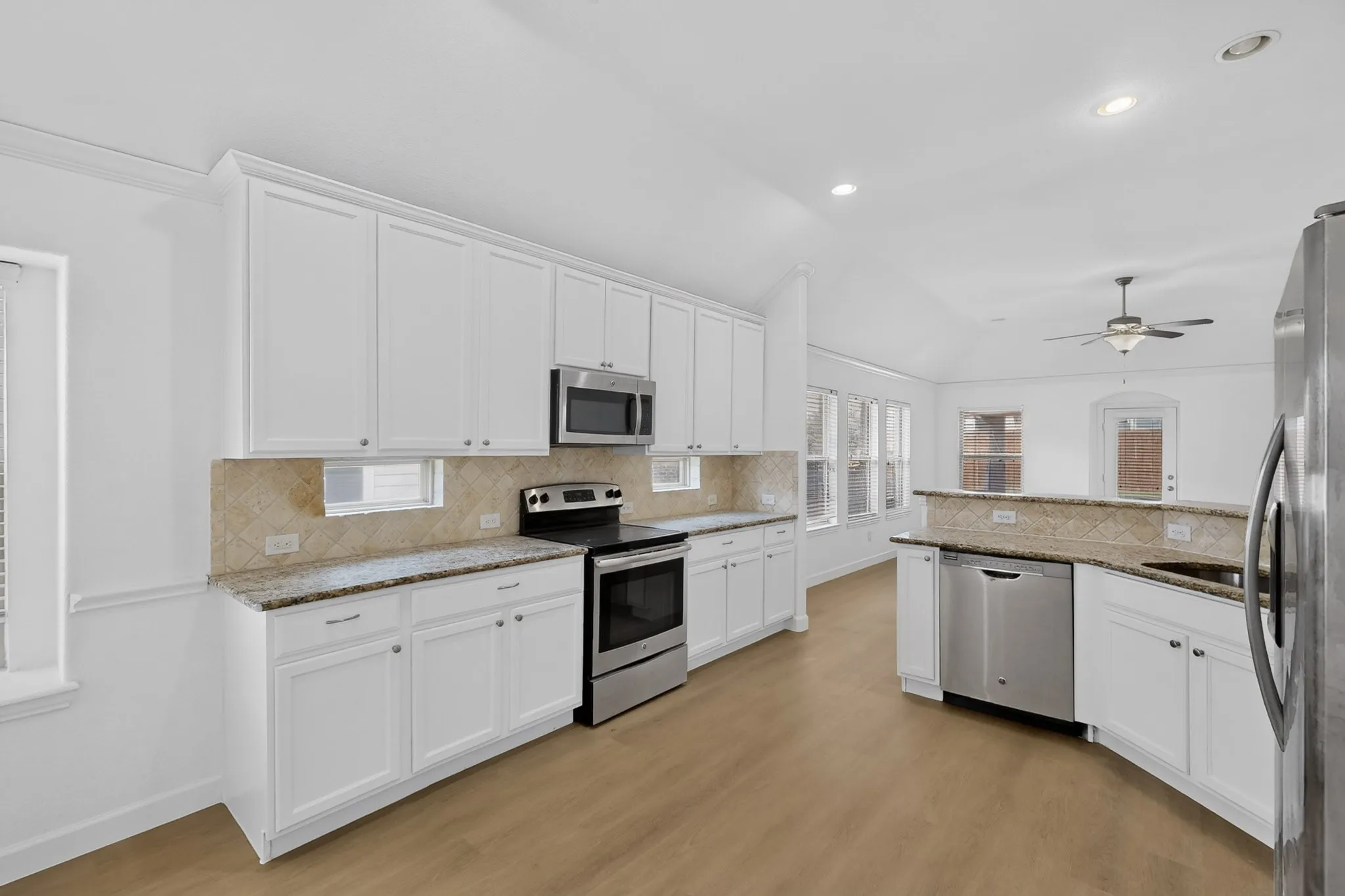 Kitchen featuring white cabinetry, stone-finish countertops, stainless steel appliances, a tiled backsplash, and wood-finish flooring