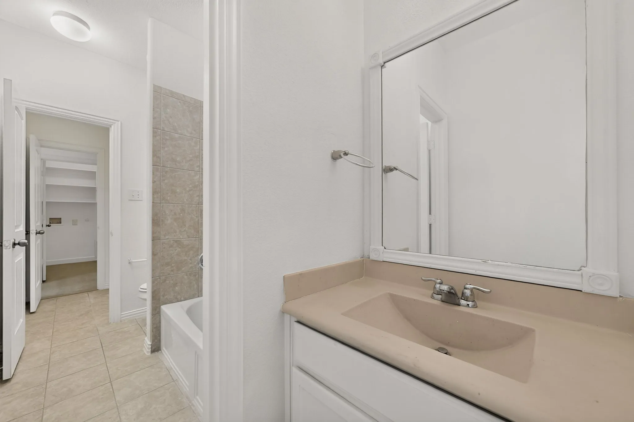 Bathroom featuring a vanity with integrated sink, framed wall-mounted mirror, ceramic tile flooring, and a bathtub with tile surround