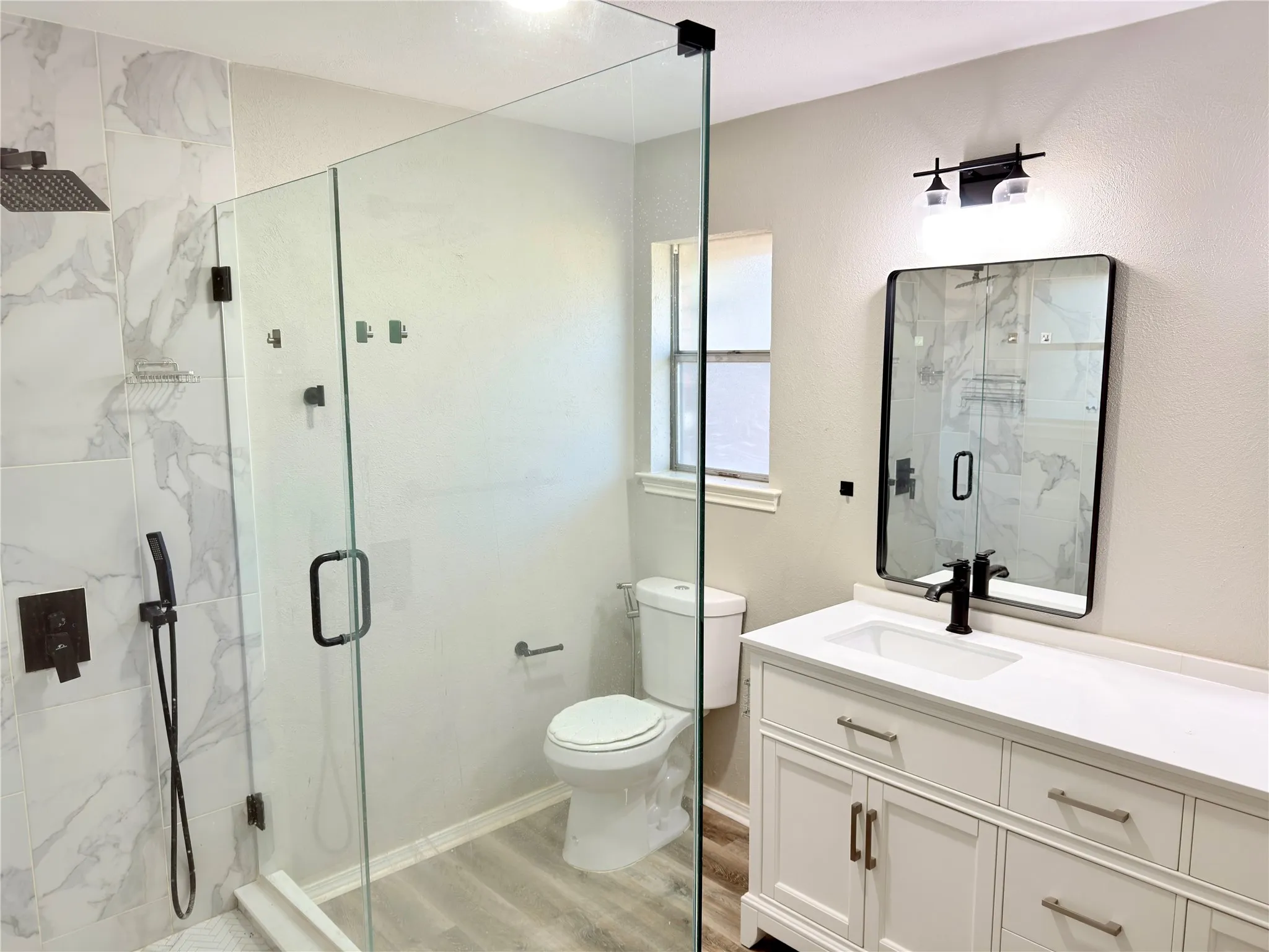 Bathroom featuring a frameless glass-enclosed shower with large-format tile surround, rainfall showerhead, and handheld sprayer