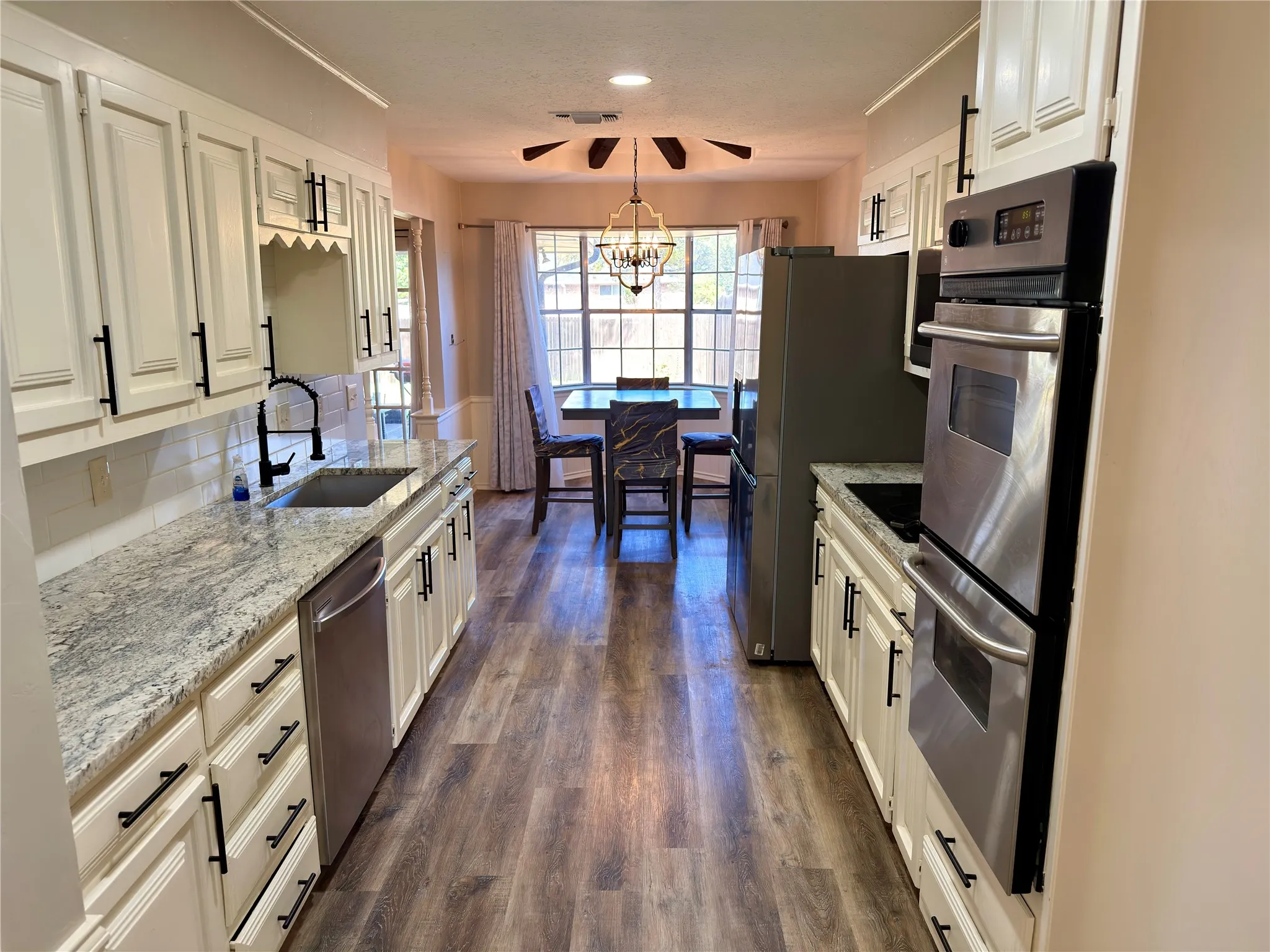 Kitchen featuring white cabinetry with matte black hardware, stone-patterned countertops, stainless steel double wall ovens, a deep under-mount sink, and wood-finish flooring