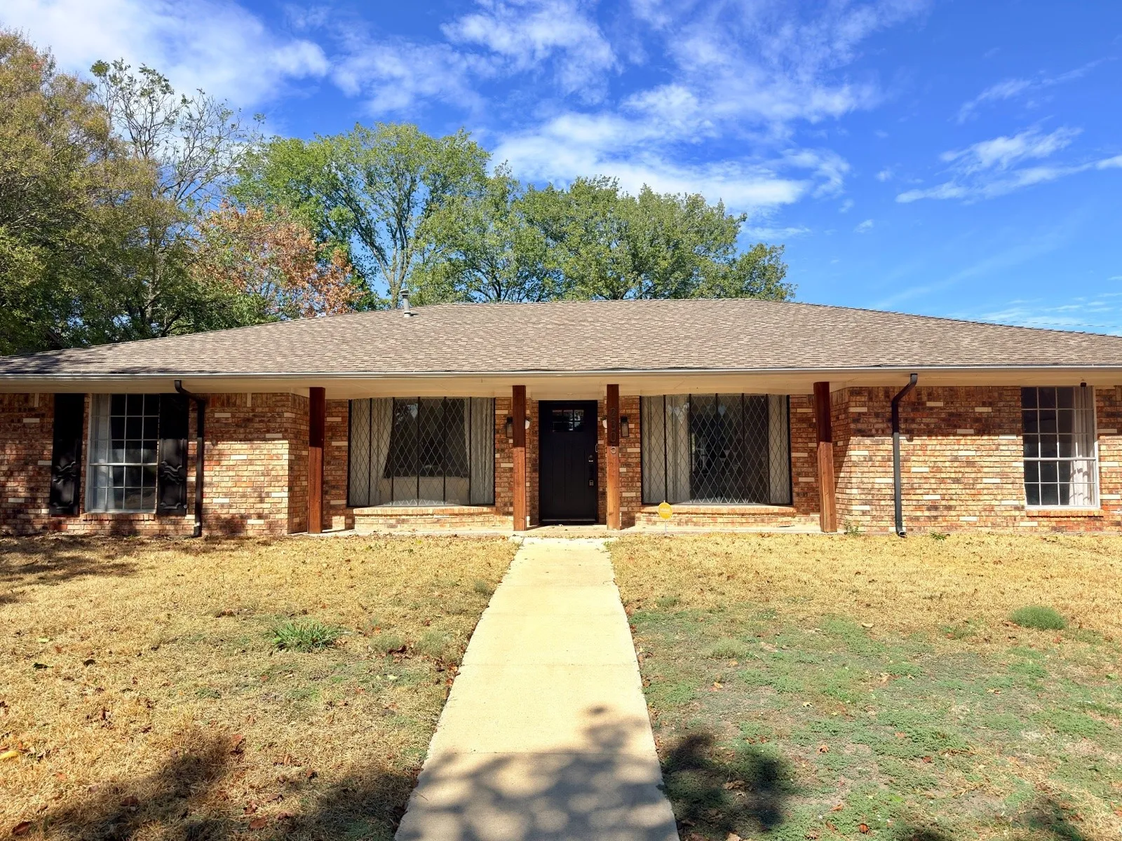 Single-story brick exterior featuring a covered front porch with wood-finish support columns, a composition shingle roof, and metal-grille window accents