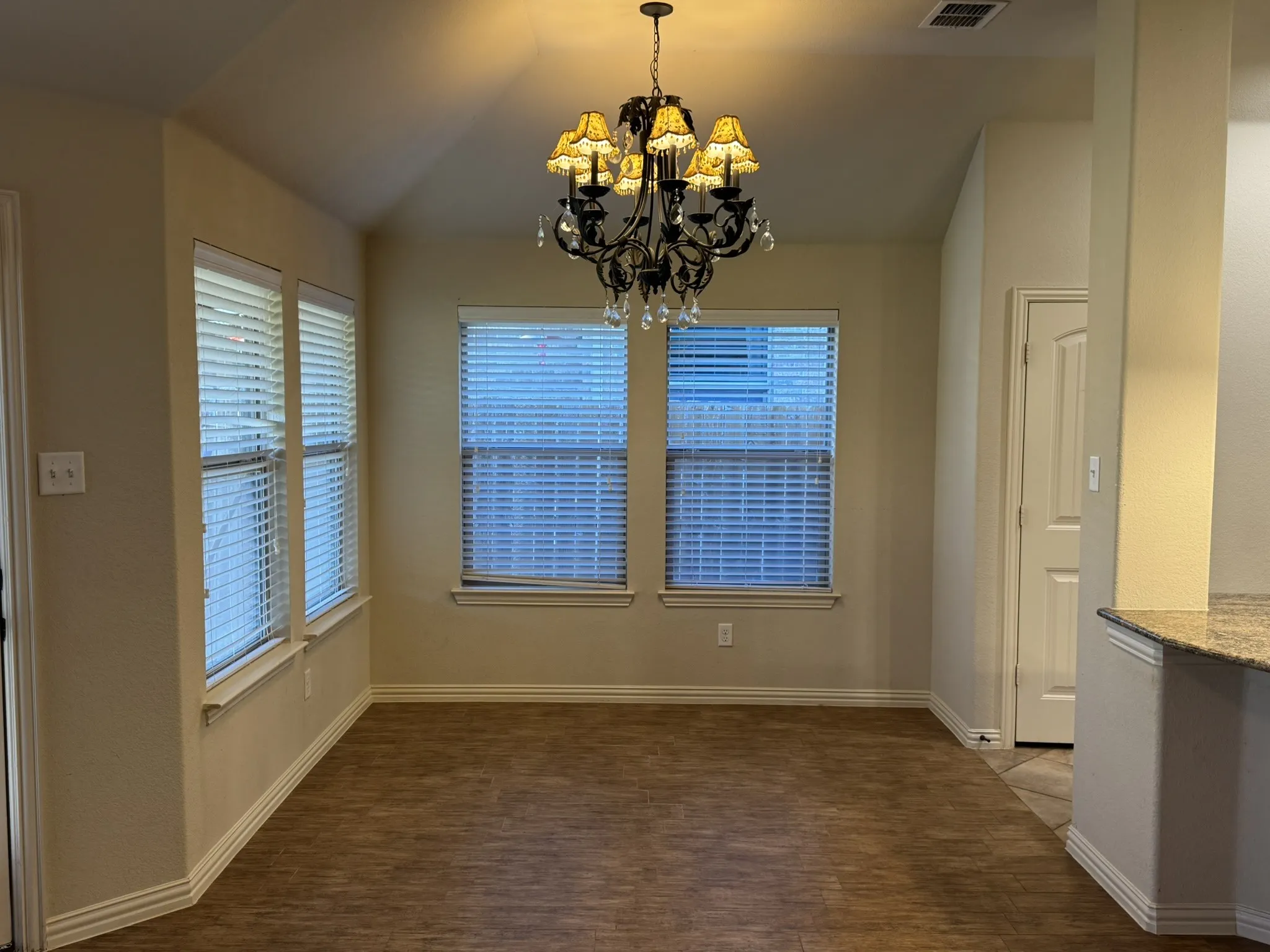 Vaulted ceiling, wood-finish flooring, multi-pane windows with horizontal blinds, and a traditional tiered chandelier