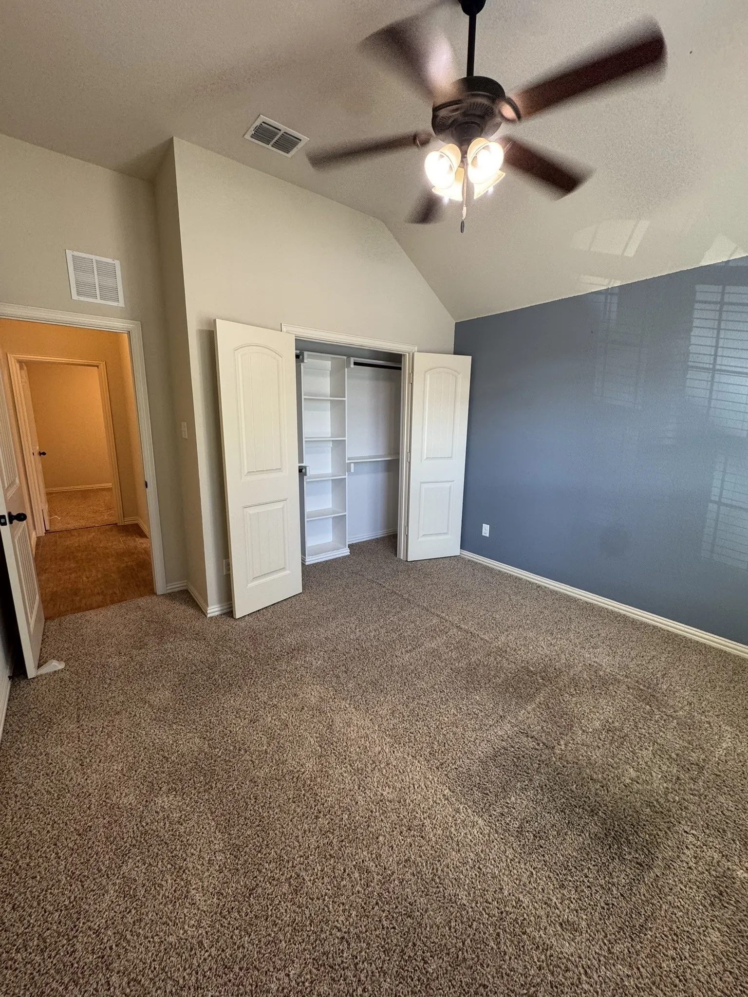 Vaulted ceilings, carpeted flooring, built-in closet shelving, and a ceiling fan with integrated lighting