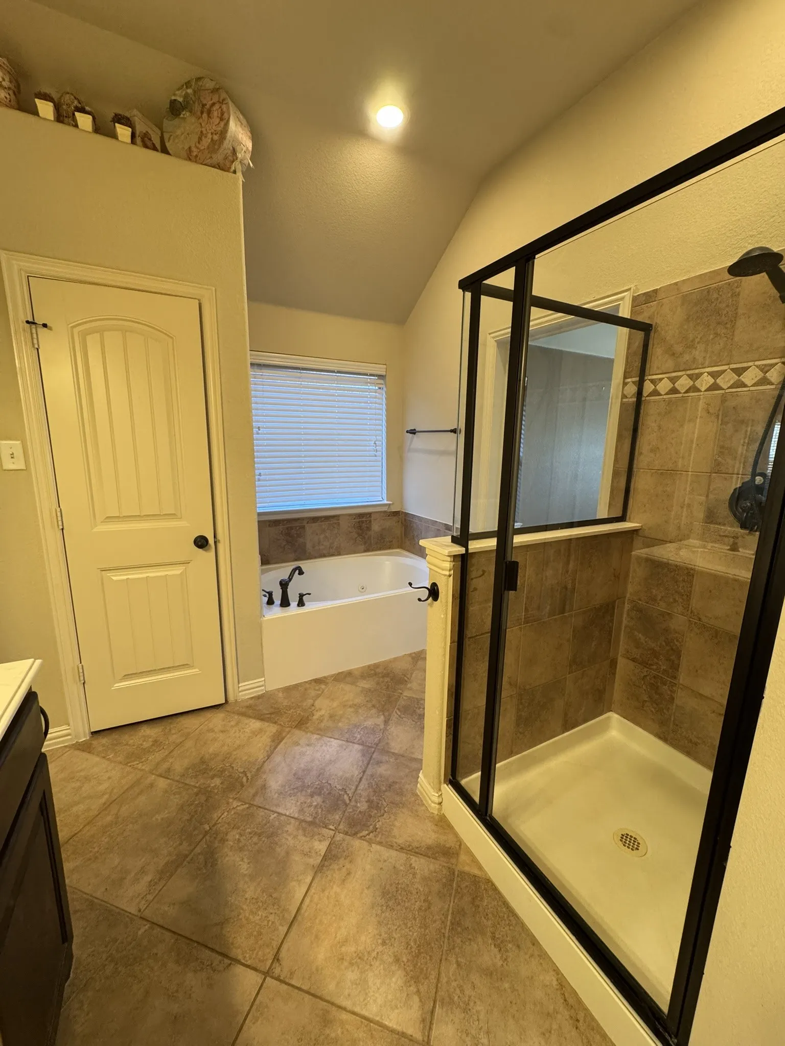Soaking tub with tile surround, glass-enclosed shower with tiled walls, and large-format tile flooring