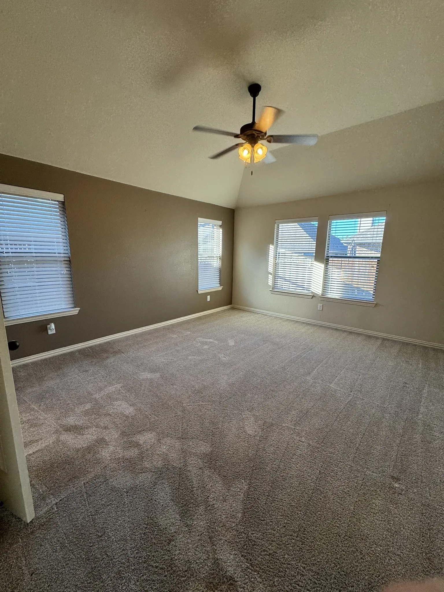 Vaulted ceiling featuring a central multi-blade ceiling fan with integrated lighting, neutral wall tones, and carpeting