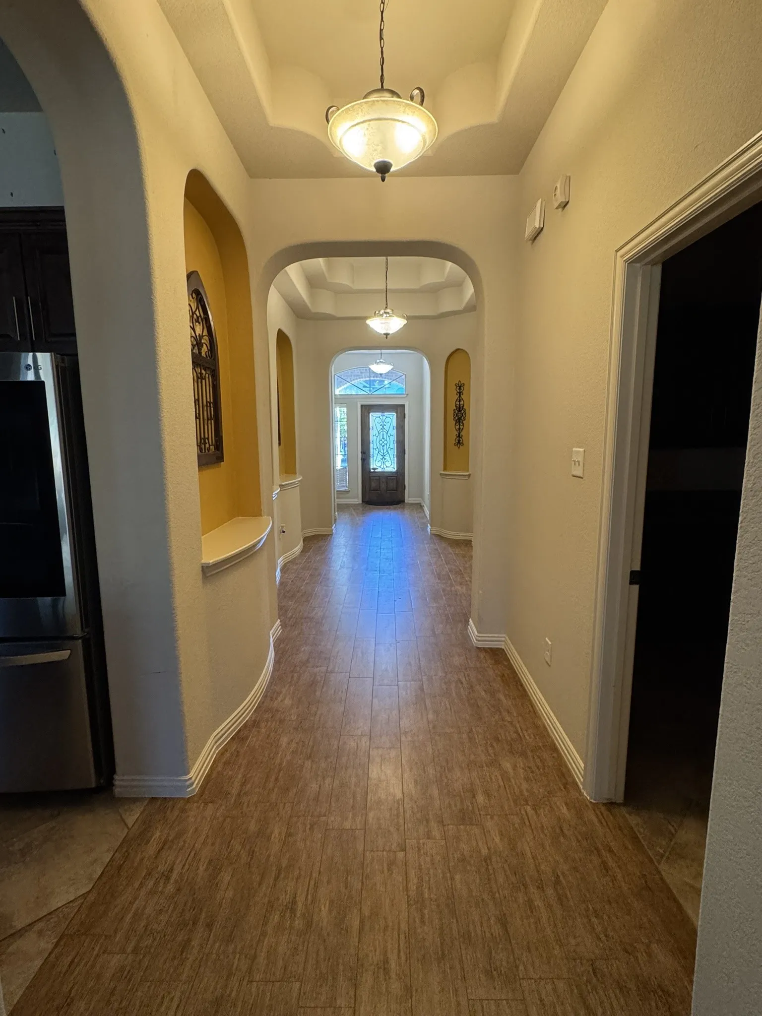 Entryway featuring wood-finish flooring, recessed ceilings, arched architectural alcoves, and decorative pendant lighting