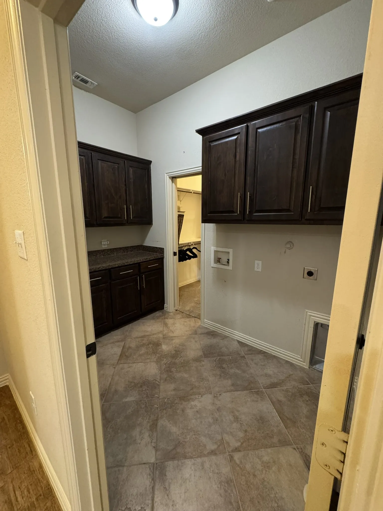 Utility room featuring dark-finish cabinetry, stone-texture countertops, tile flooring, and wall-mounted storage units