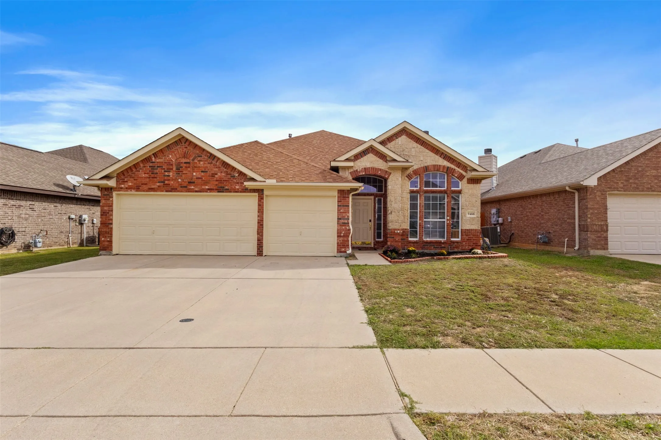 Single-story brick and masonry exterior featuring an arched entryway, gabled rooflines, decorative stonework accents, and a three-car garage