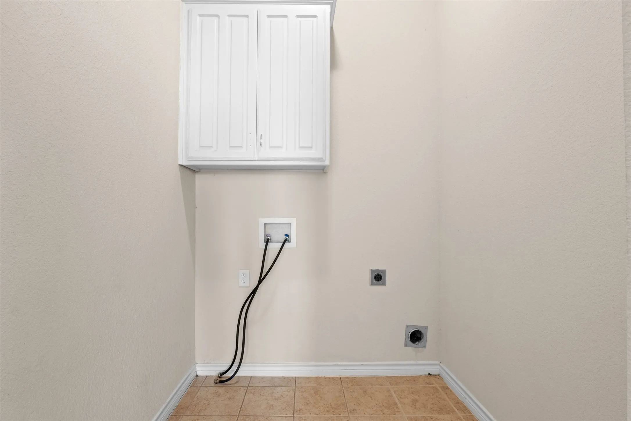 Wall-mounted white shaker-style cabinetry, ceramic tile flooring, and dedicated laundry utility hookups