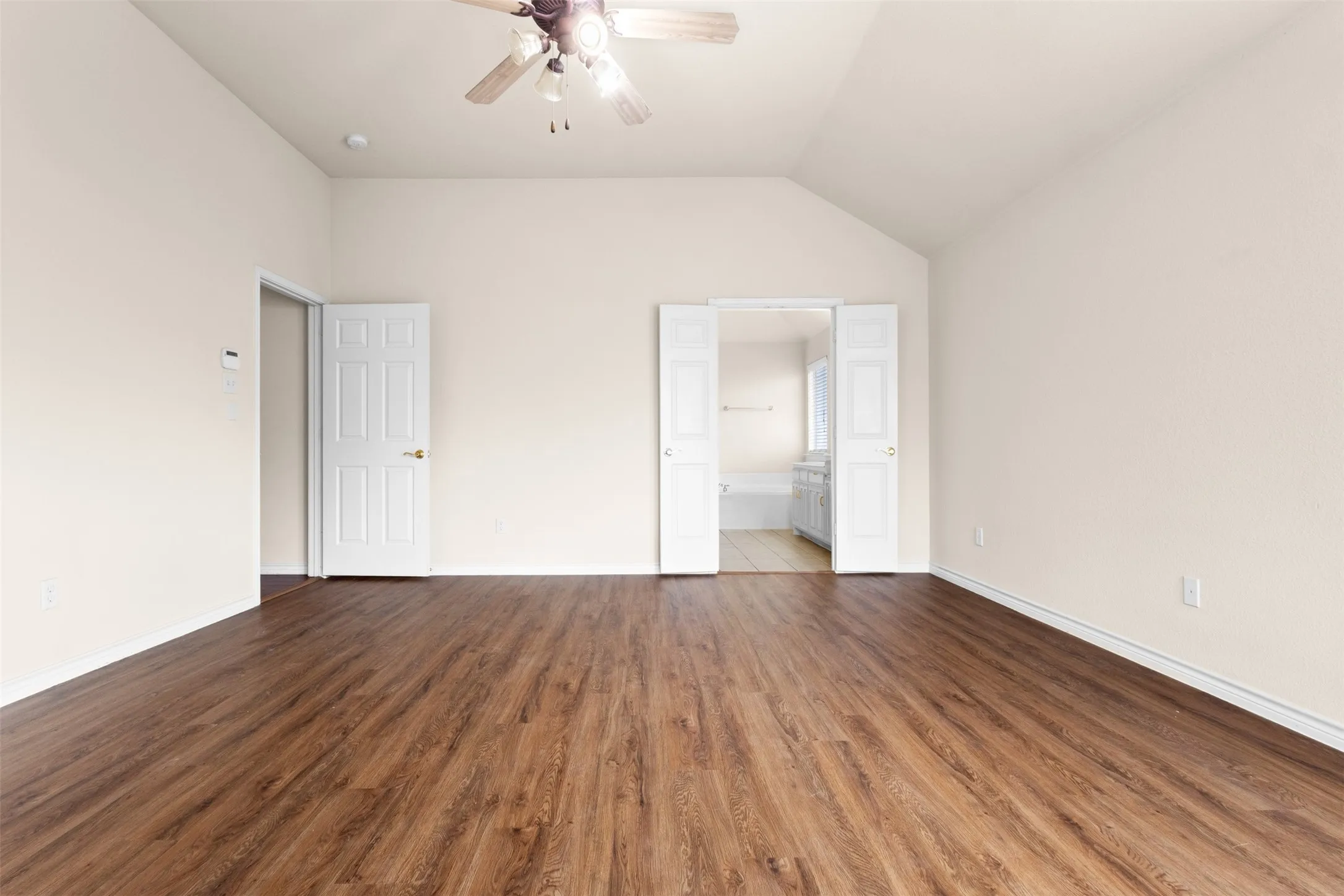 Room featuring vaulted ceilings, wood-finish flooring, a ceiling fan, and white paneled doors