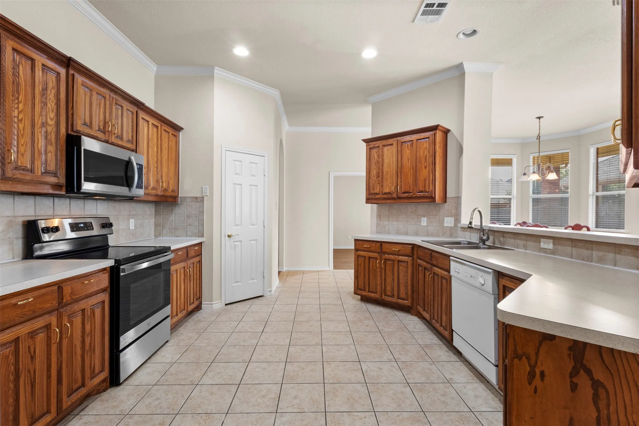Kitchen featuring stained wood cabinetry, ceramic tile flooring, stainless steel range with overhead microwave, solid-surface countertops, and tiled backsplash