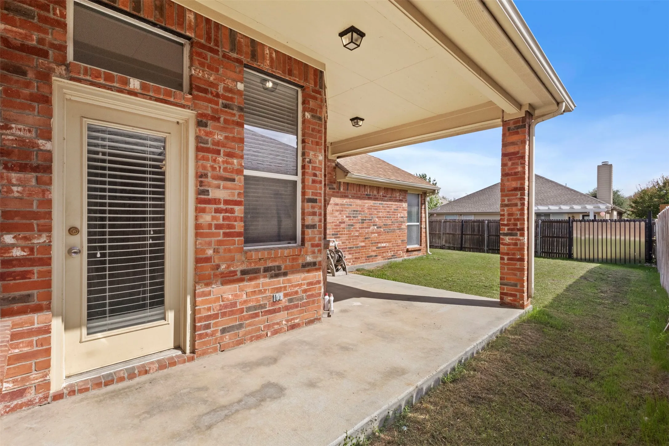 Covered concrete patio featuring red brick exterior siding, recessed ceiling lighting, and a single-light glass panel door with a transom window