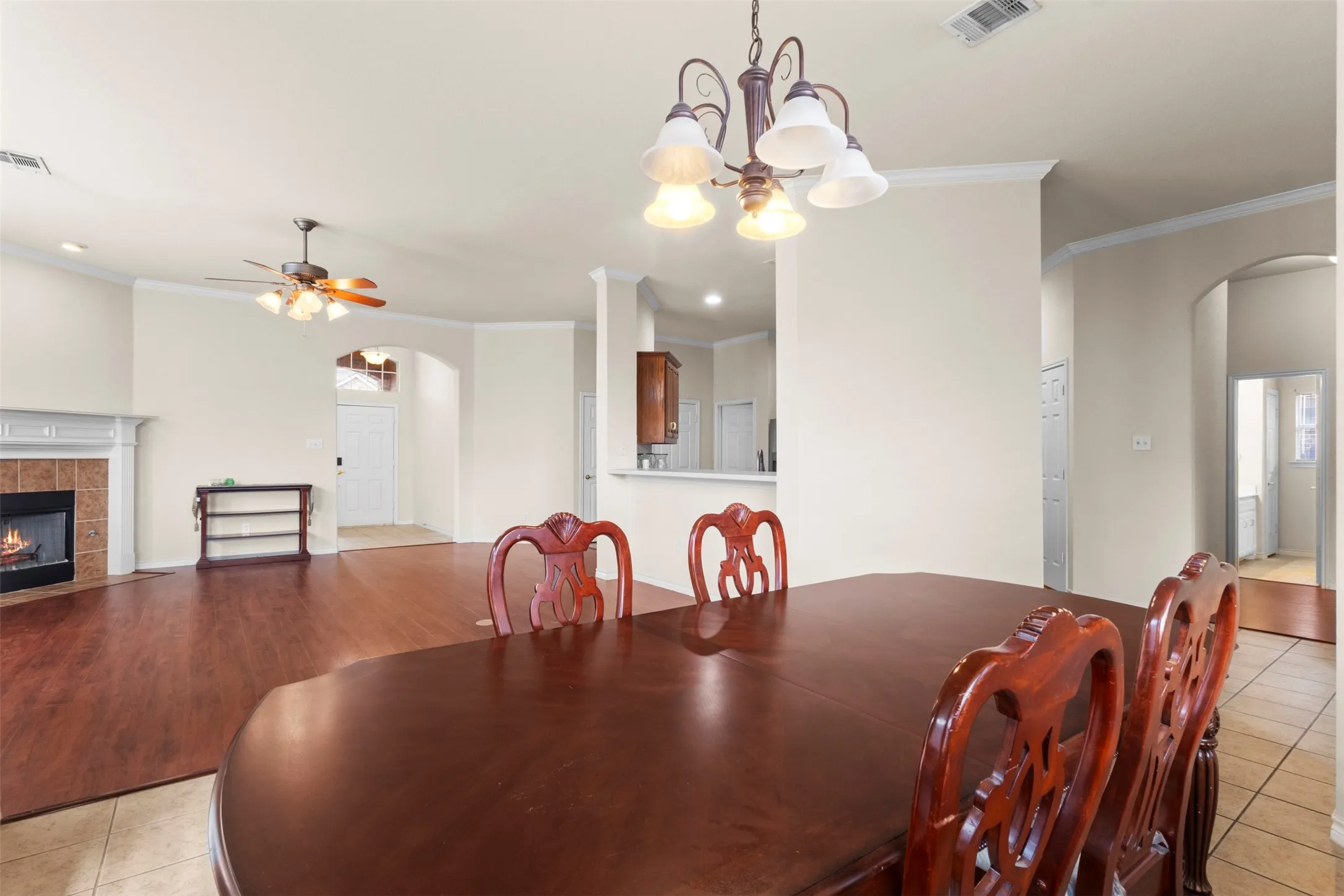 Open floor plan featuring wood-finish flooring, a fireplace with a mantel and tiled surround, crown molding, and a suspended chandelier