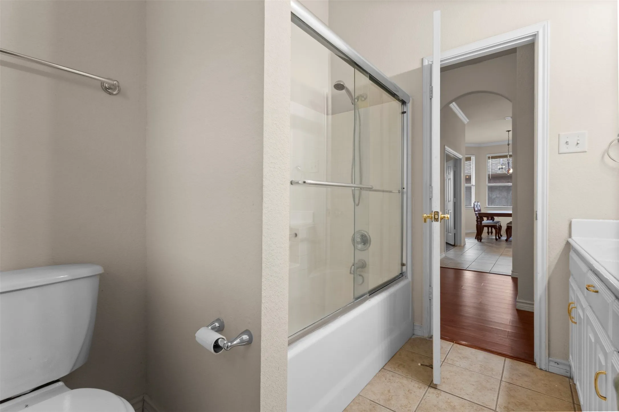 Bathroom featuring a bathtub with a sliding glass enclosure, a white vanity with hardware, tiled flooring, and a towel bar
