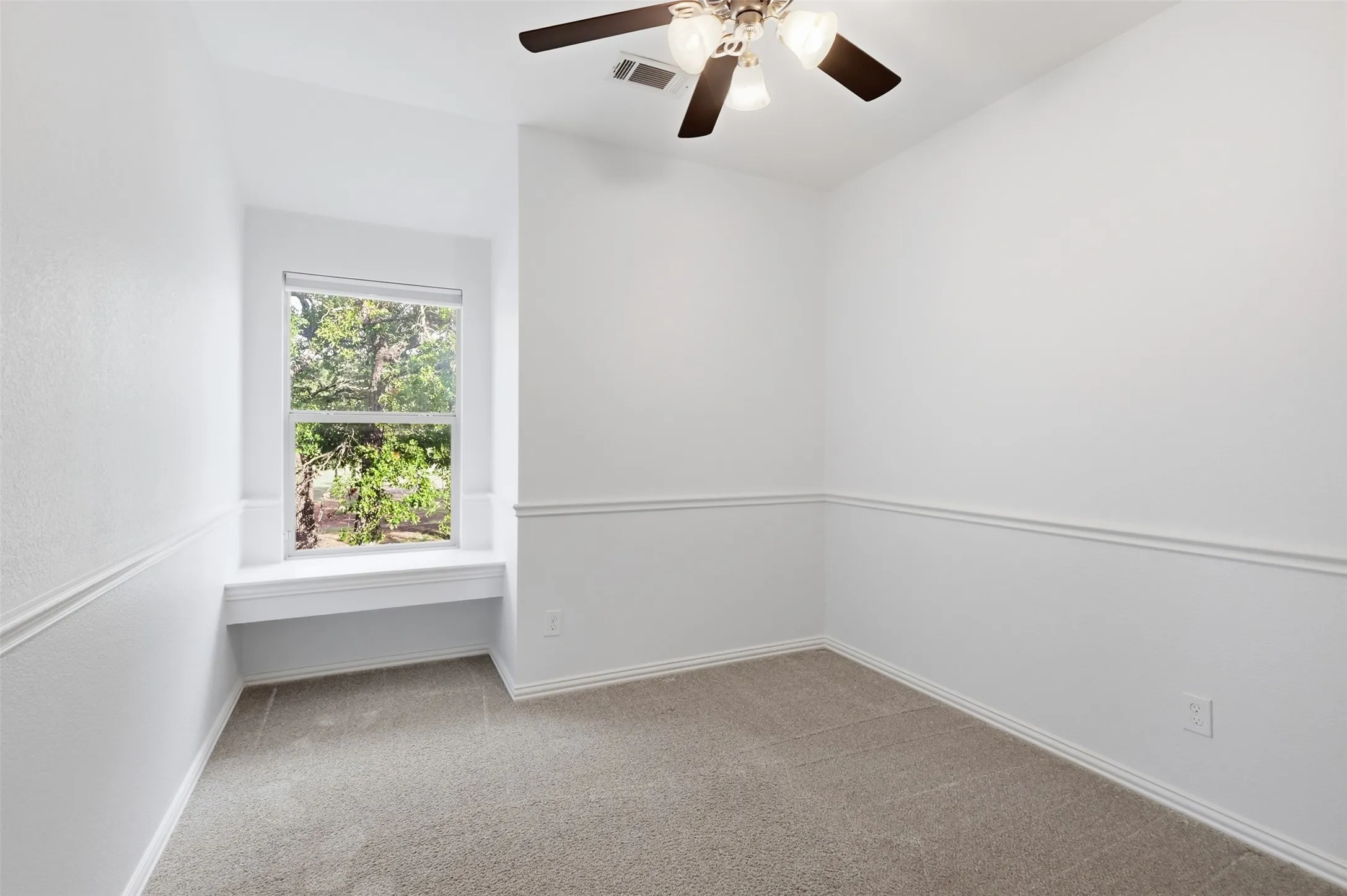 Interior room featuring neutral carpeting, a built-in window seat, chair rail molding, and a ceiling fan with integrated lighting