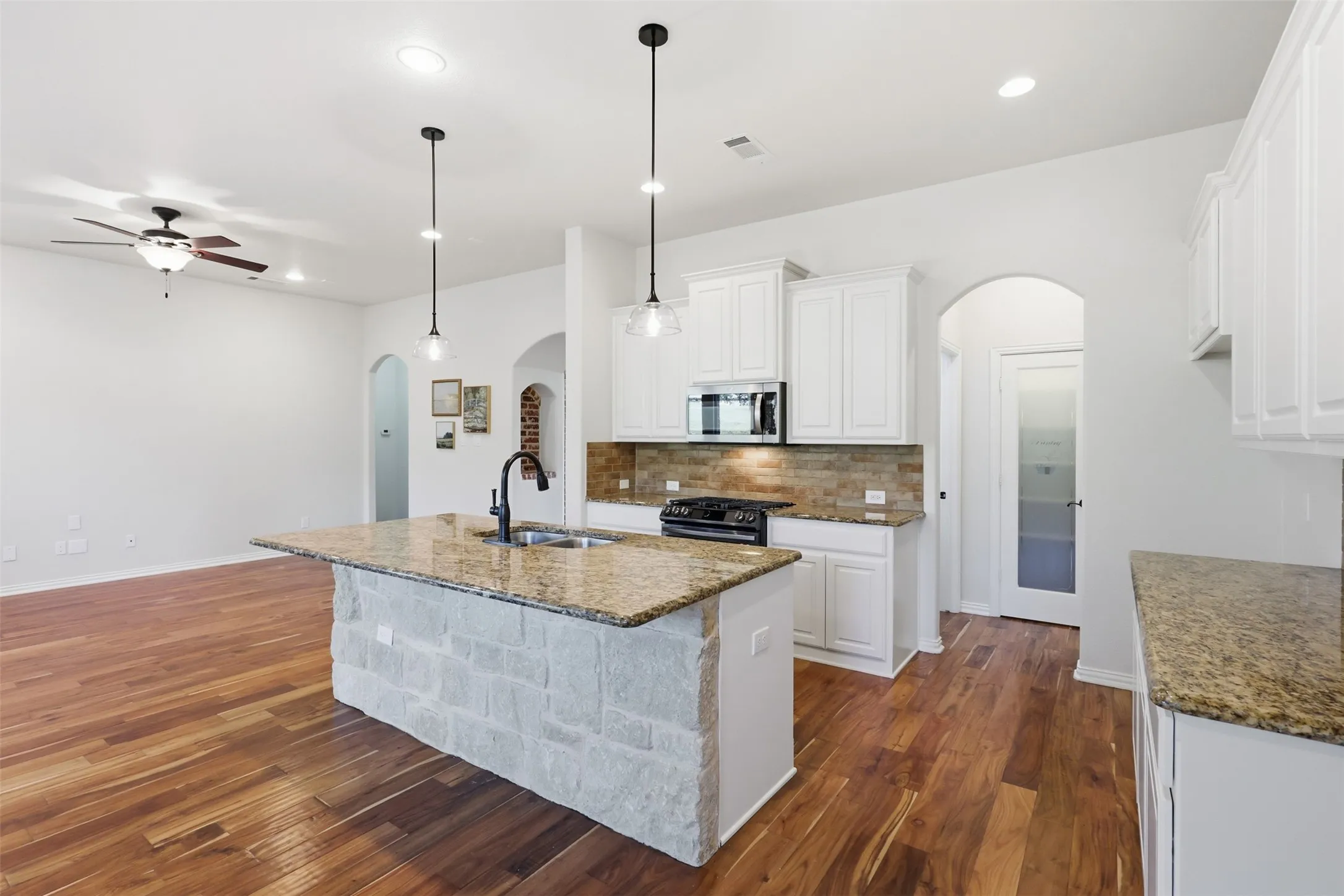 Kitchen featuring a center island with a stone base and stone-finish countertop, wood-finish flooring, white shaker-style cabinetry, and a stone backsplash