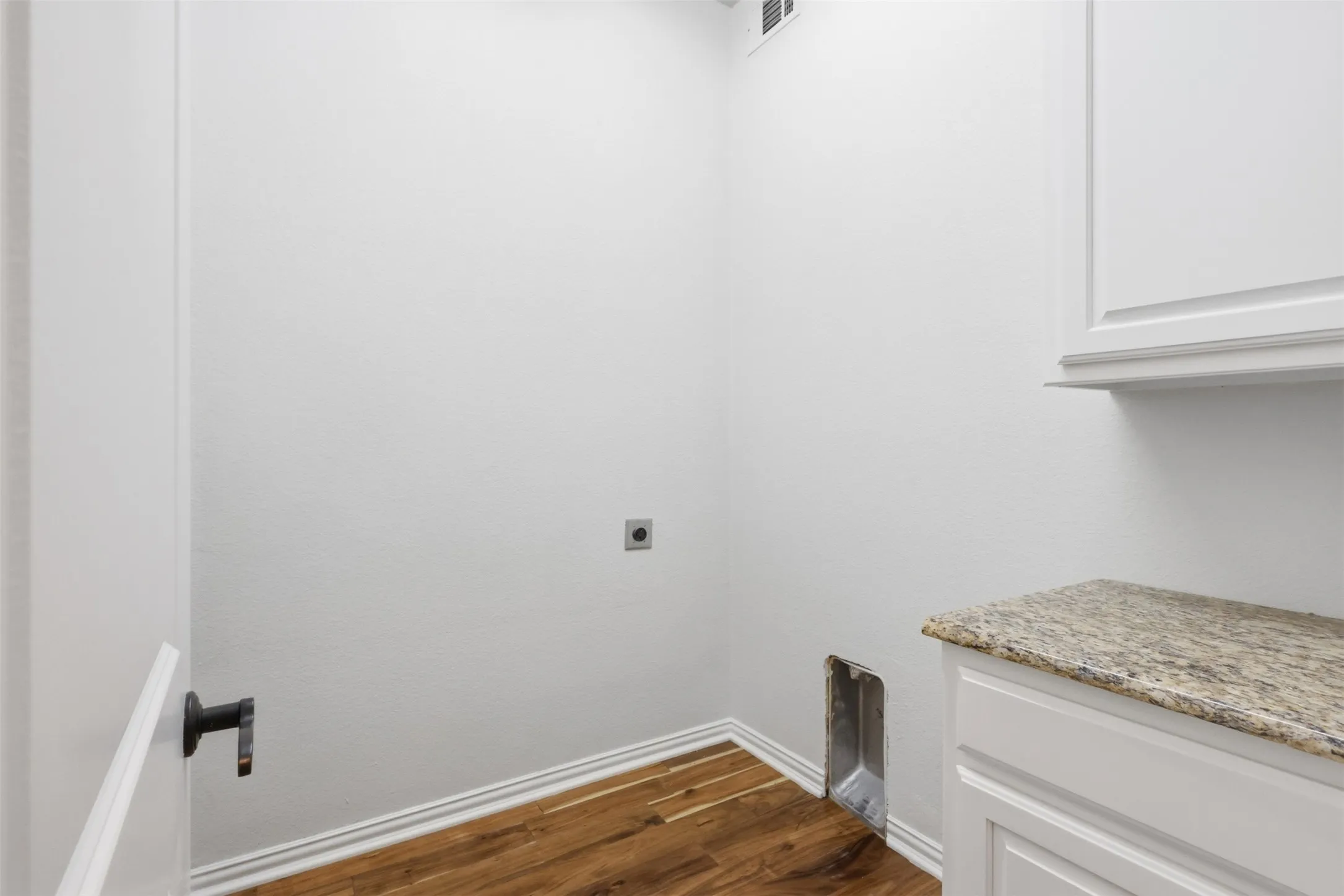 Utility area featuring wood-finish flooring, stone-surfaced countertop, built-in white cabinetry, and matte black hardware