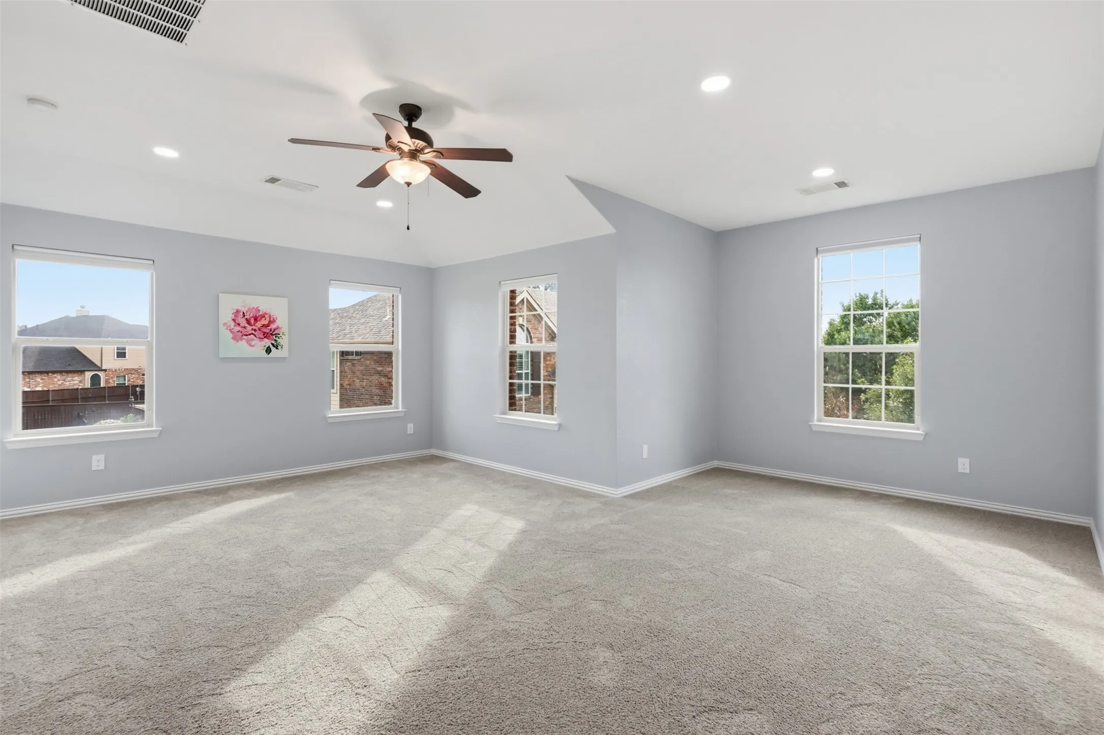 Spacious room featuring a vaulted ceiling, recessed lighting, neutral carpeting, and a multi-blade ceiling fan