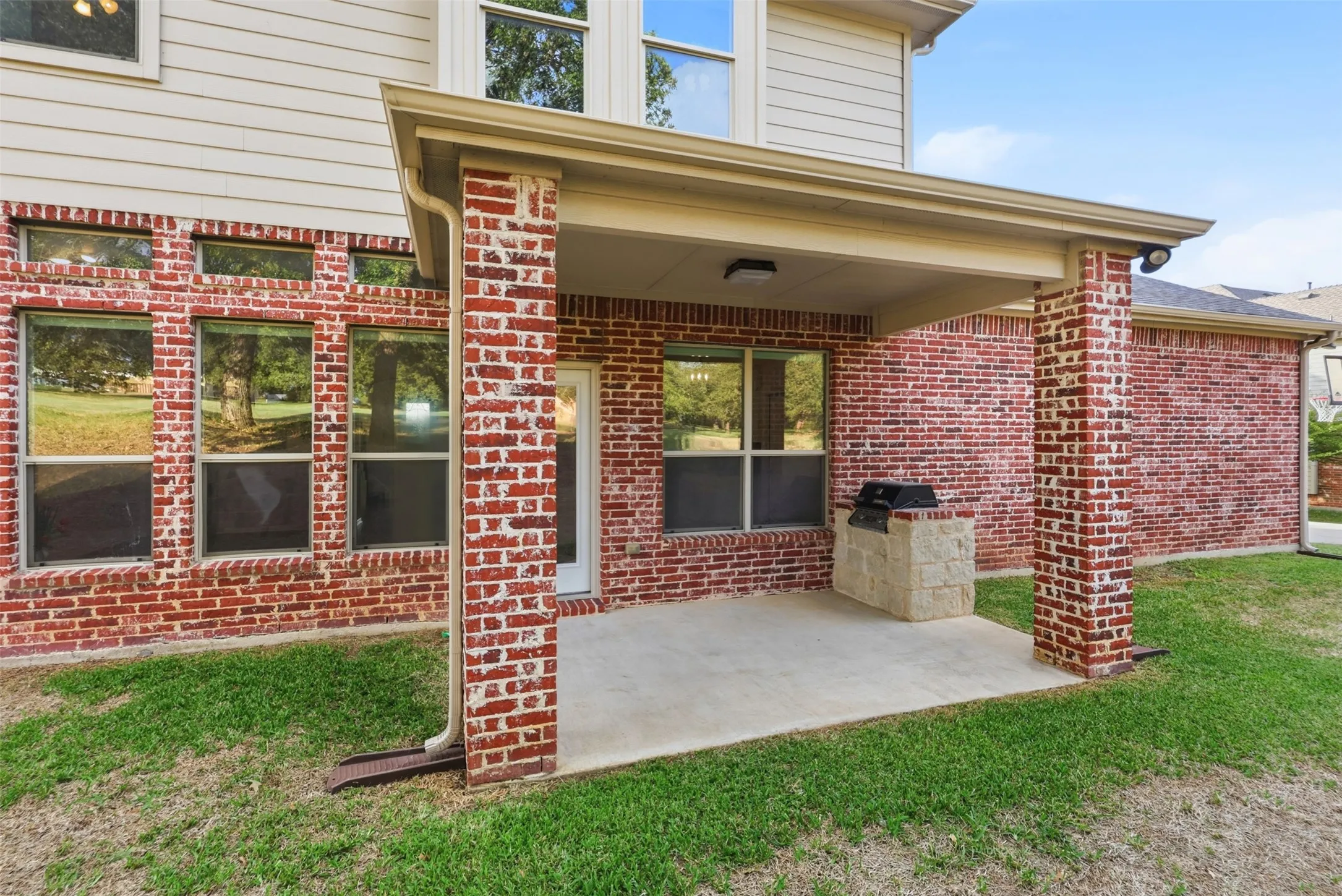 Covered rear patio featuring brick columns, concrete flooring, and a built-in stone grill station