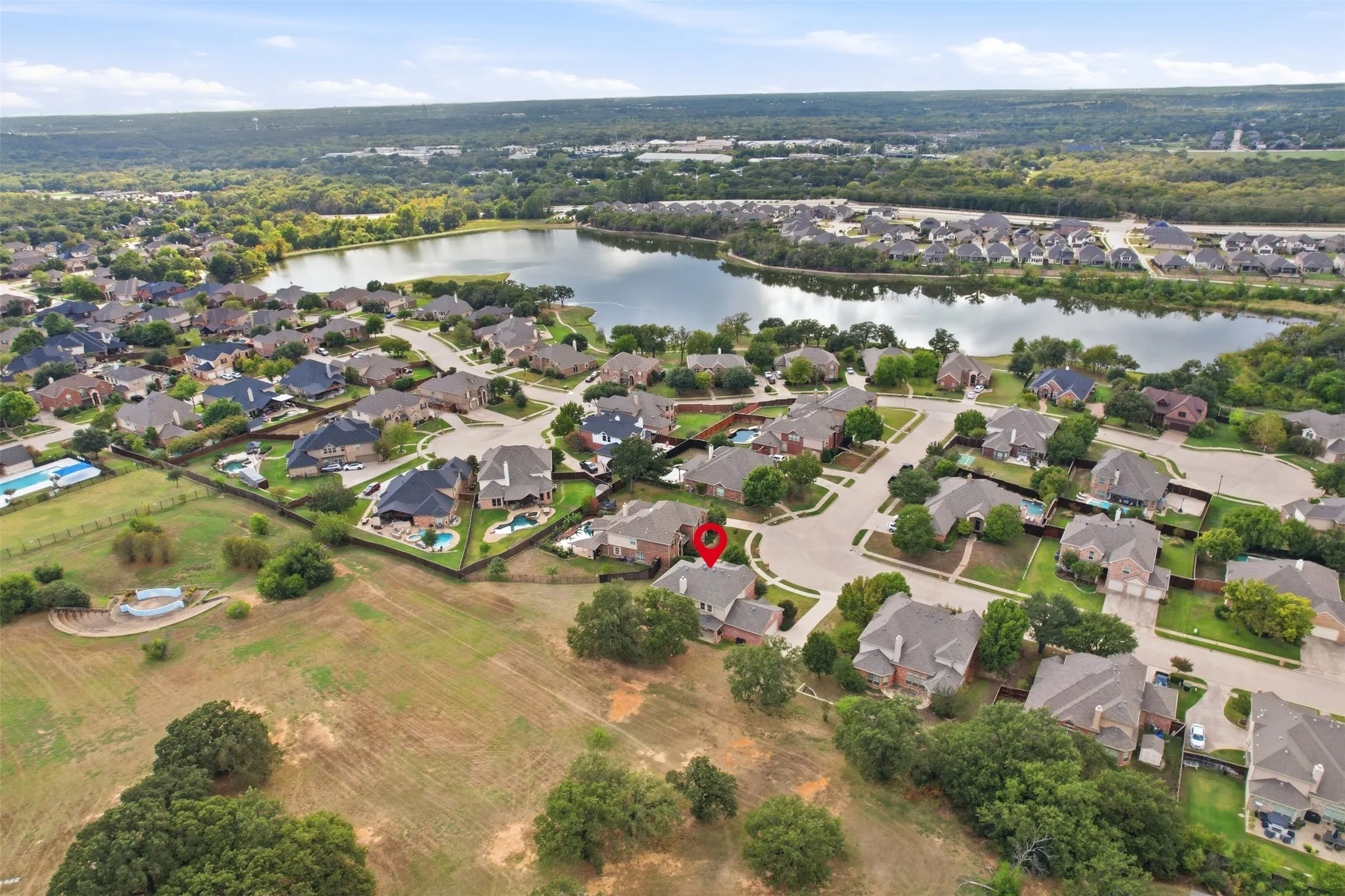 Aerial perspective of residential property featuring a multi-pitched roofline, expansive open terrain, mature trees, and proximity to a large water feature
