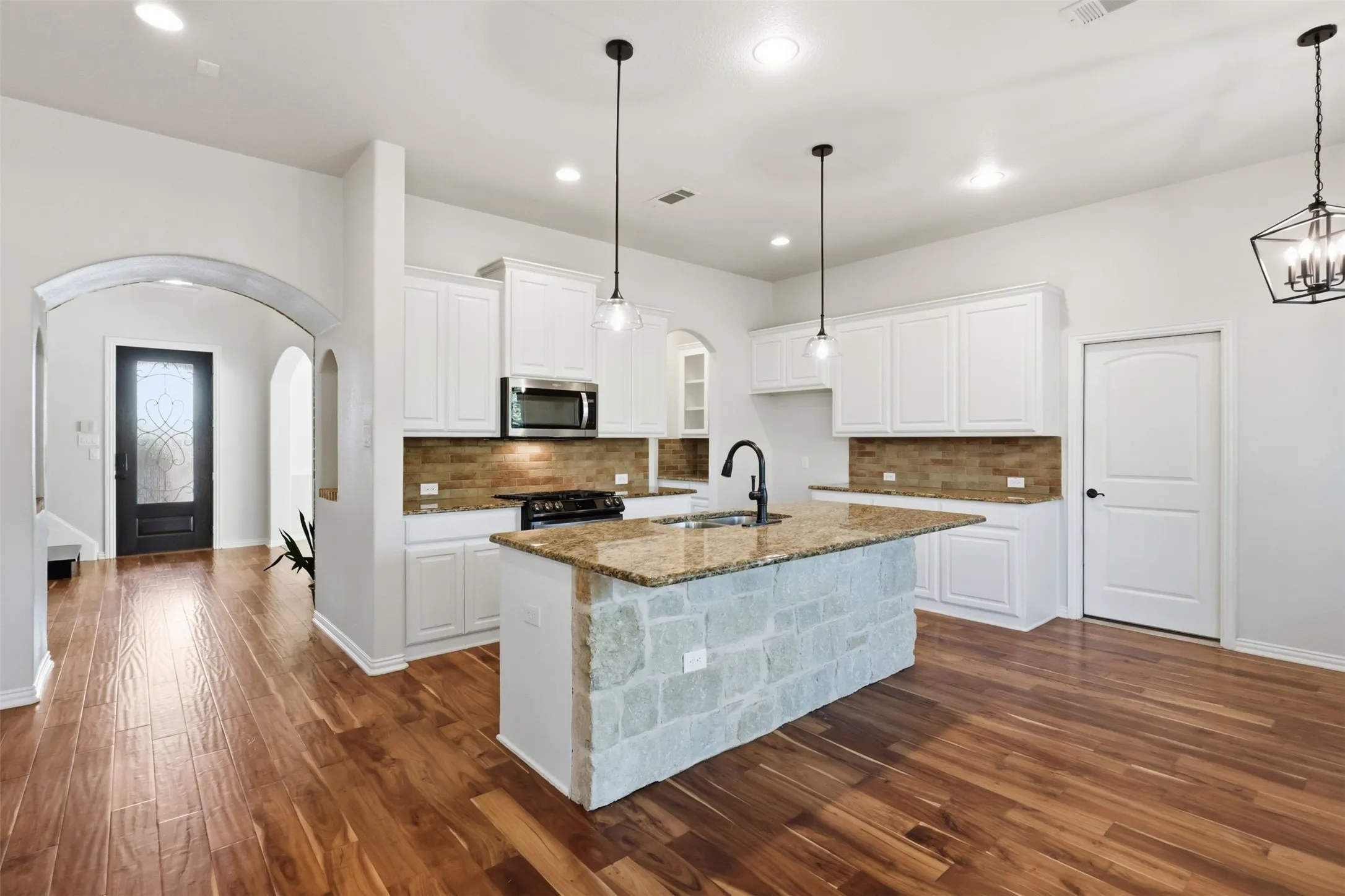 Kitchen featuring white cabinetry, stone-clad island base, wood-finish flooring, stone-tiled backsplash, and geometric pendant lighting