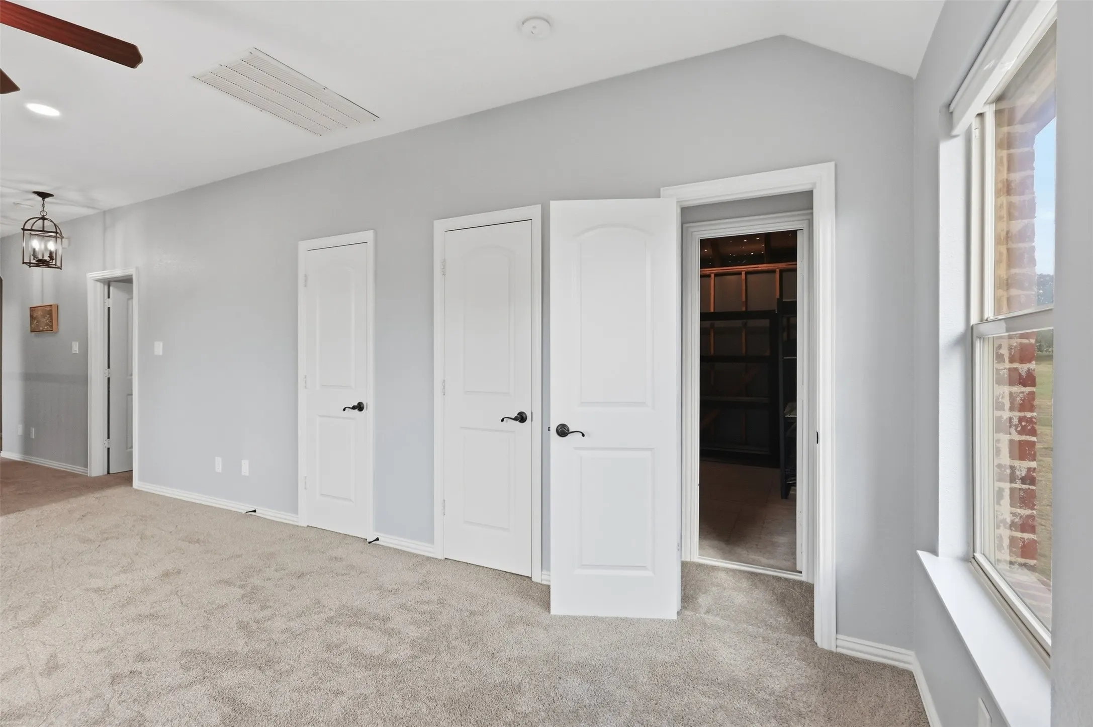 Vaulted ceilings with recessed lighting, neutral carpeting, three-panel interior doors with matte black hardware, and an expansive window with a brick exterior surround