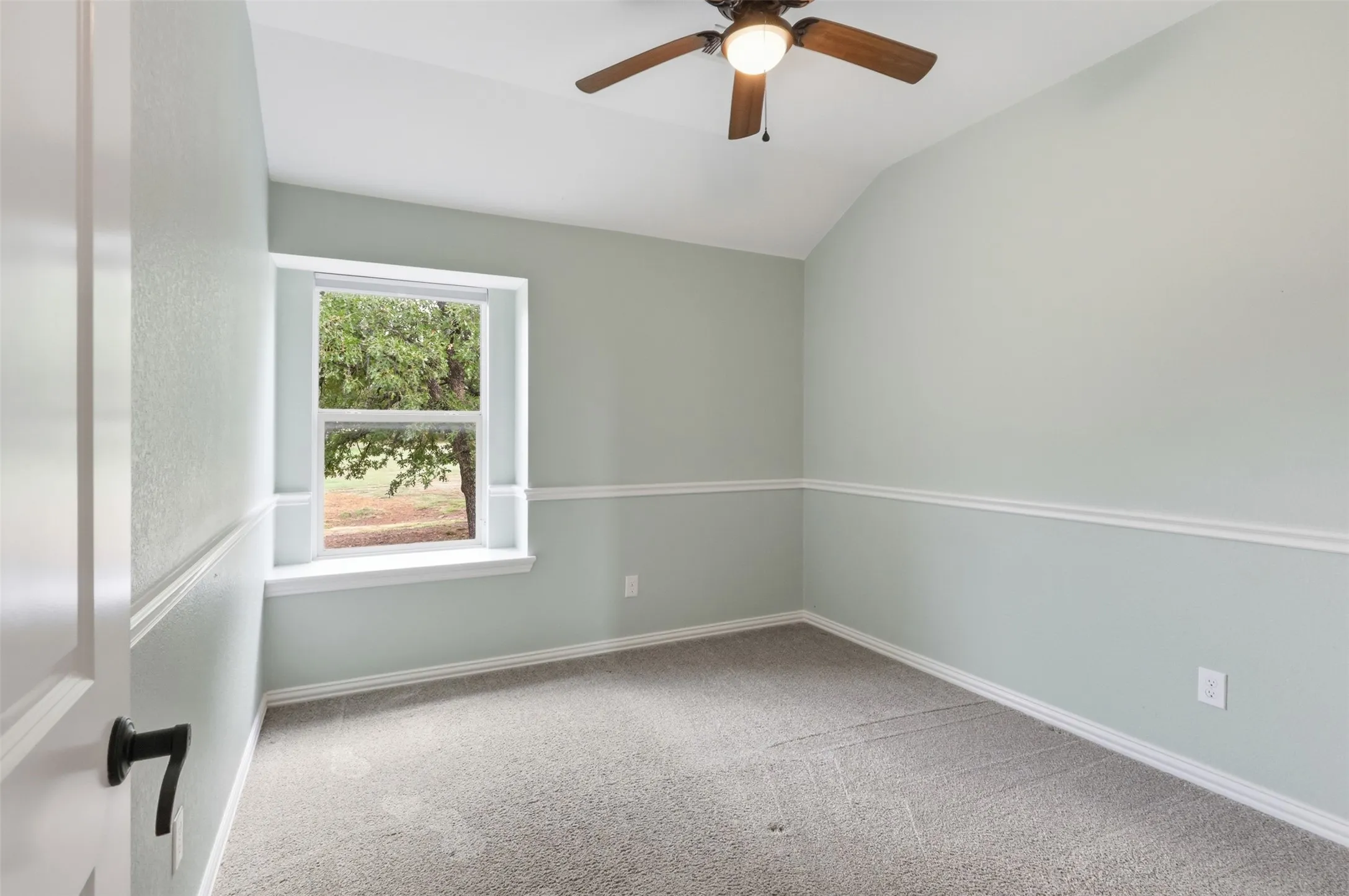 Interior room featuring a vaulted ceiling, neutral wall-to-wall carpeting, decorative chair rail molding, and a built-in ceiling fan with integrated lighting